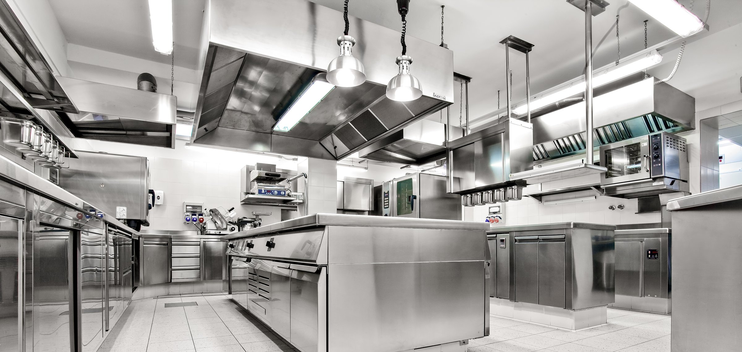 Spacious commercial kitchen with ovens, stoves, prep counters, and ventilation hoodsideal for high-volume culinary operations.