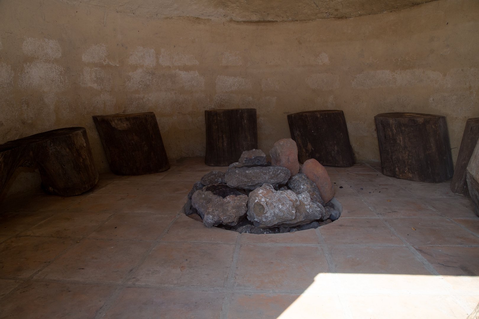 Interior view of a traditional mexican temazcal, featuring a circular pit filled with volcanic stones and surrounded by wooden log seats