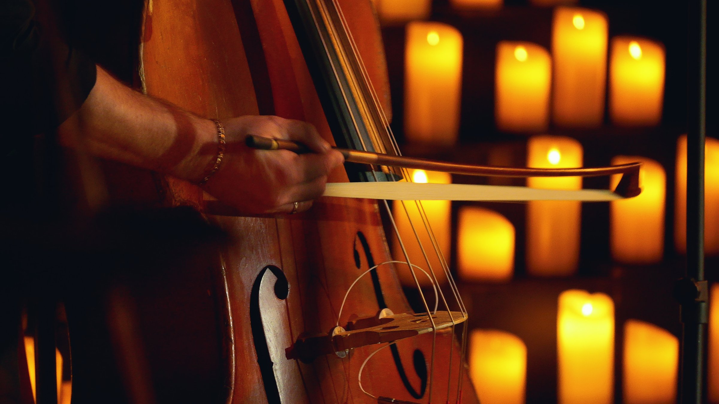 Close-up of a musician playing the double bass on a stage surrounded by candles