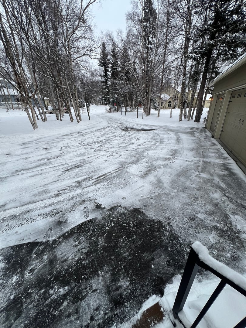 Residential snow clearing service showcasing a cleared driveway and walkway in a snowy Anchorage neighborhood, surrounded by trees and homes.
