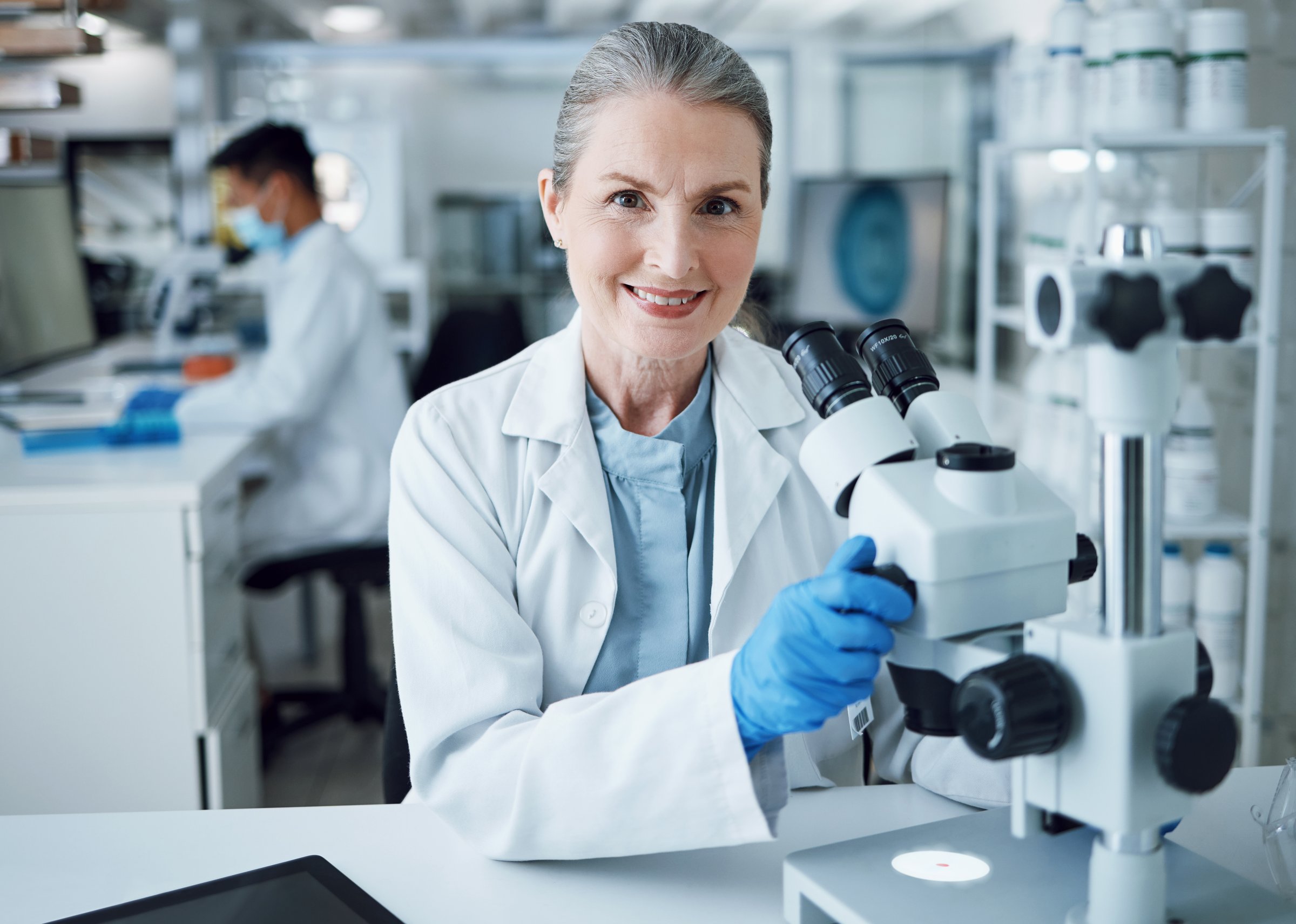 Microscope, scientist and portrait of senior woman in laboratory to review virus research, medical test and biotechnology. Science, microbiology and happy female professor planning expert assessment