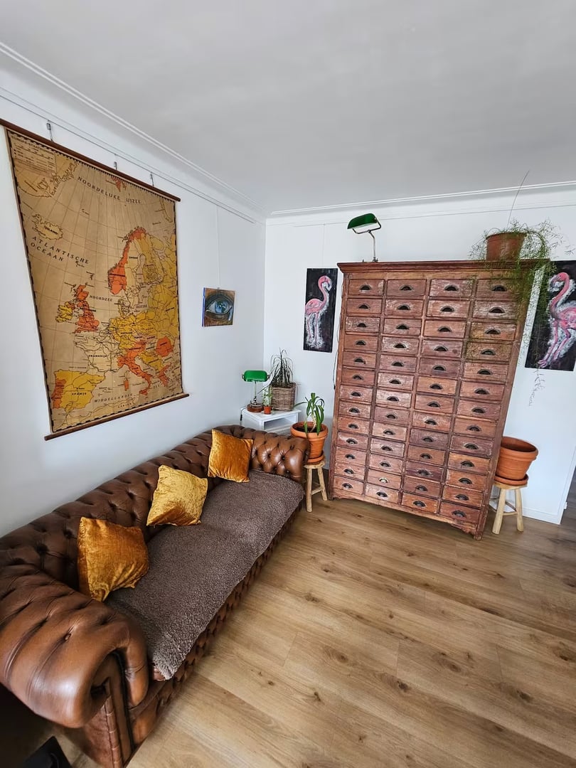 Vintage-style room with a brown leather sofa, large wooden cabinet, European map, and flamingo art on white walls.