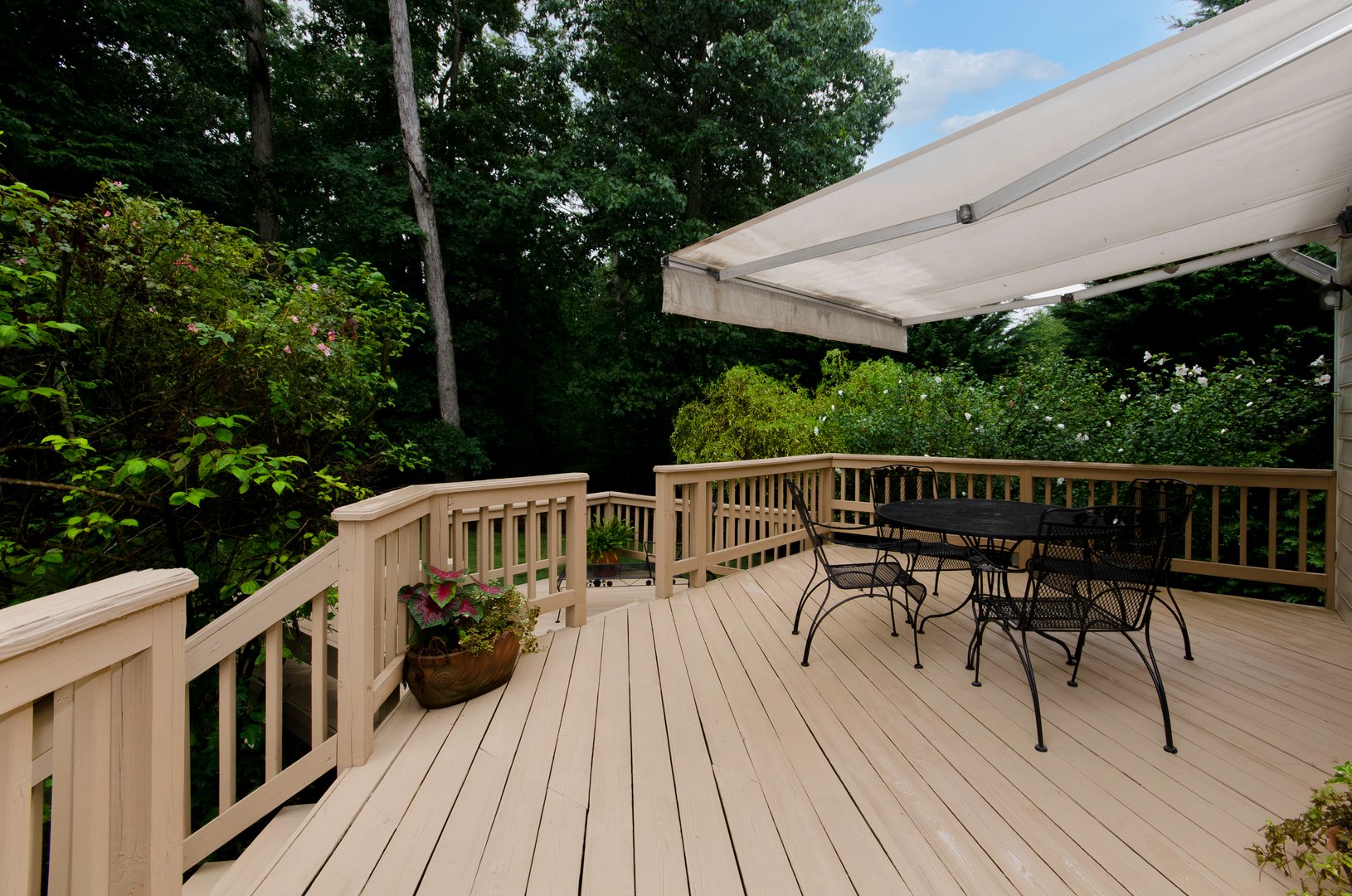 A spacious wooden deck with an awning, outdoor furniture, surrounded by lush greenery