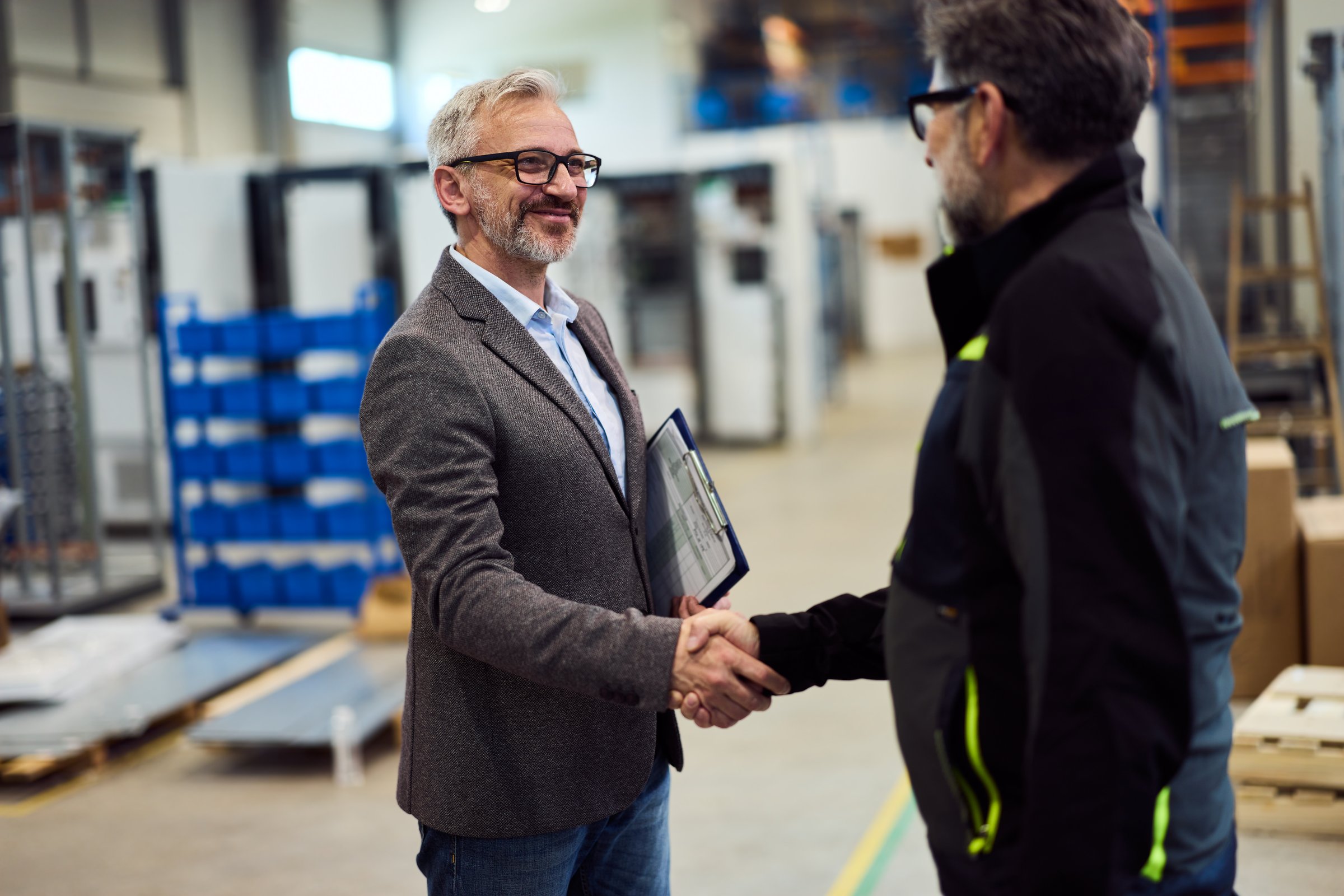 Two professionals in a factory handshake, symbolizing agreement and collaboration.