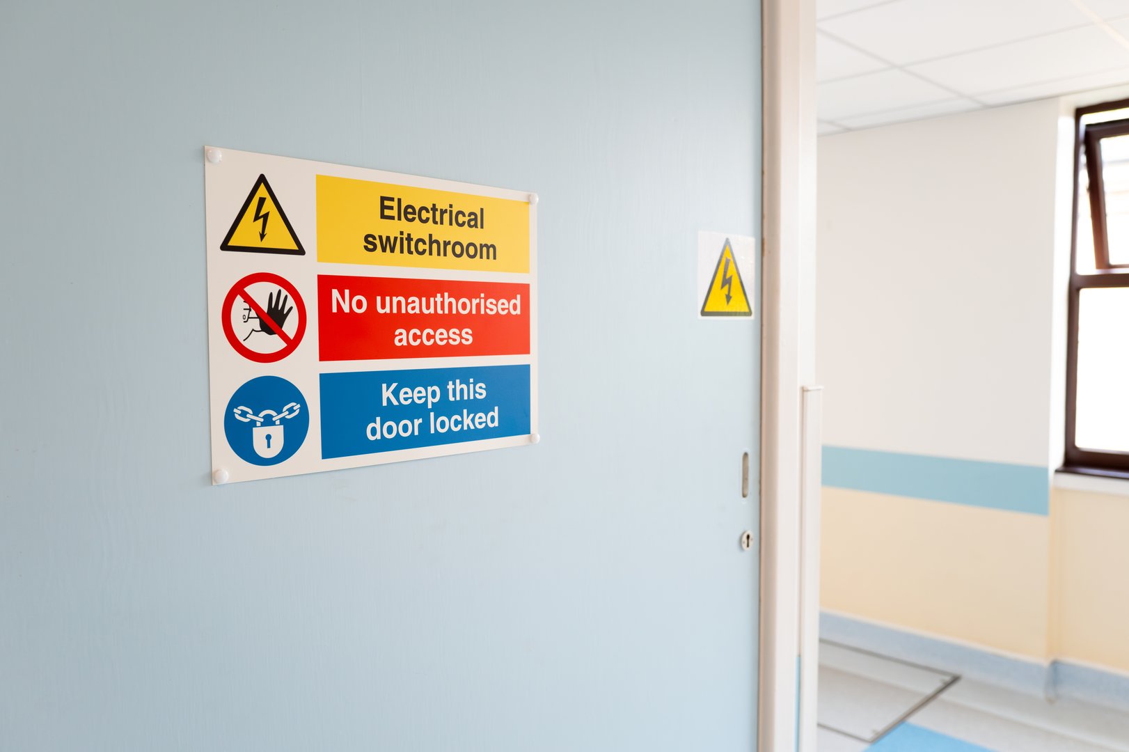 Electrical warning sign seen on the access door to X-Ray equipment located in an NHS hospital. Part of the hospital corridor is visible.