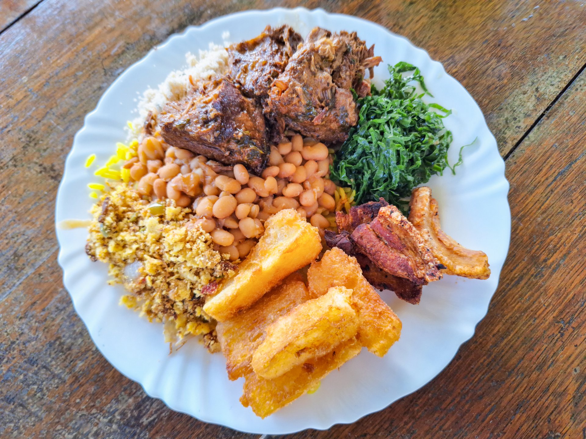 Assorted Brazilian dishes served on a white plate, including beans, rice, fried cassava, collard greens, farofa, and seasoned meat. Perfect for authentic cuisine, homemade meals, and cultural food photography.