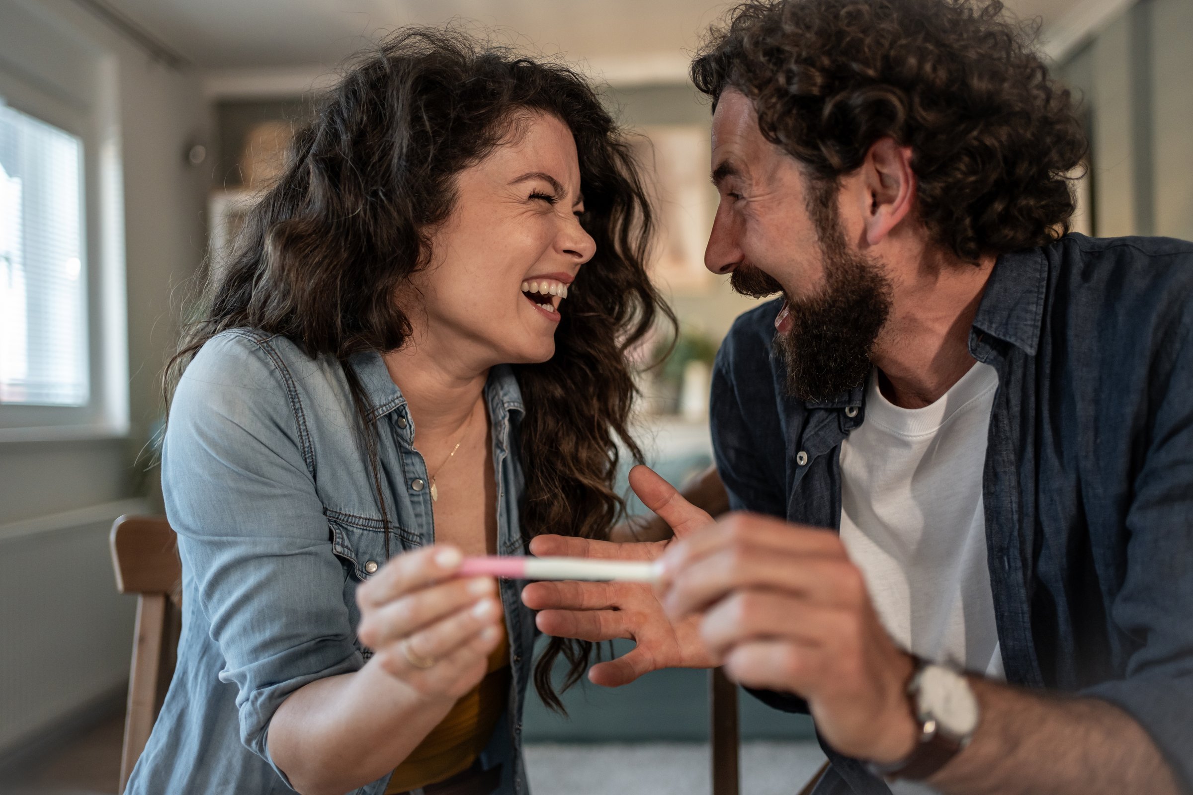 Young couple holding positive pregnancy test and laughing, celebrating the news of expecting a baby, expressing joy and excitement for the future