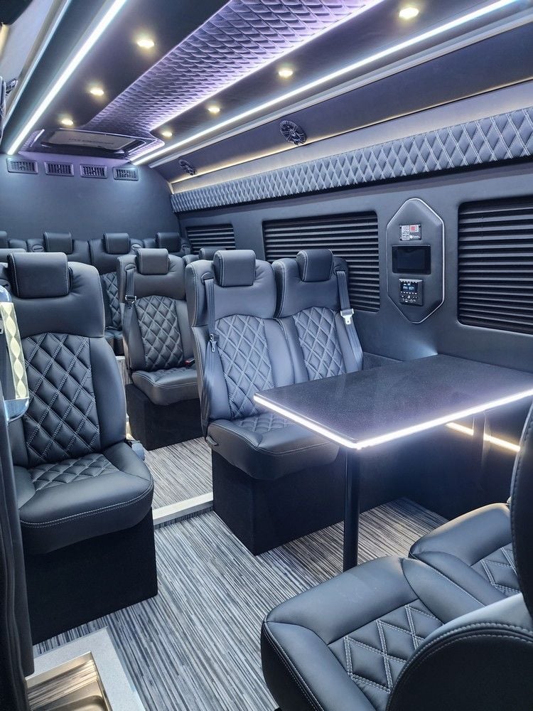 Luxurious van interior with quilted leather seats, ambient lighting, and a small table against a sleek, modern design.