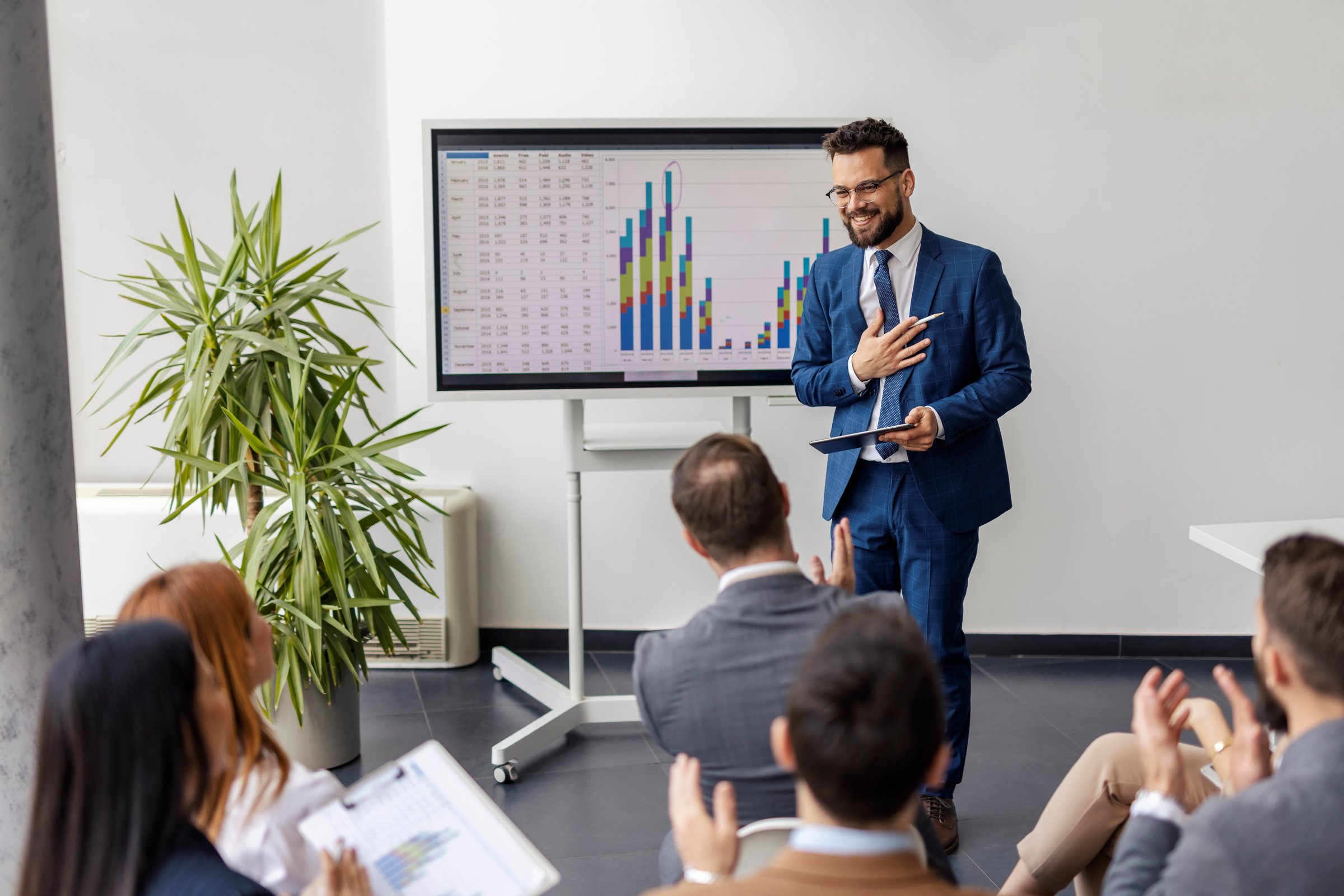 An educator standing in front of audience who are clapping hands on seminar at conference.