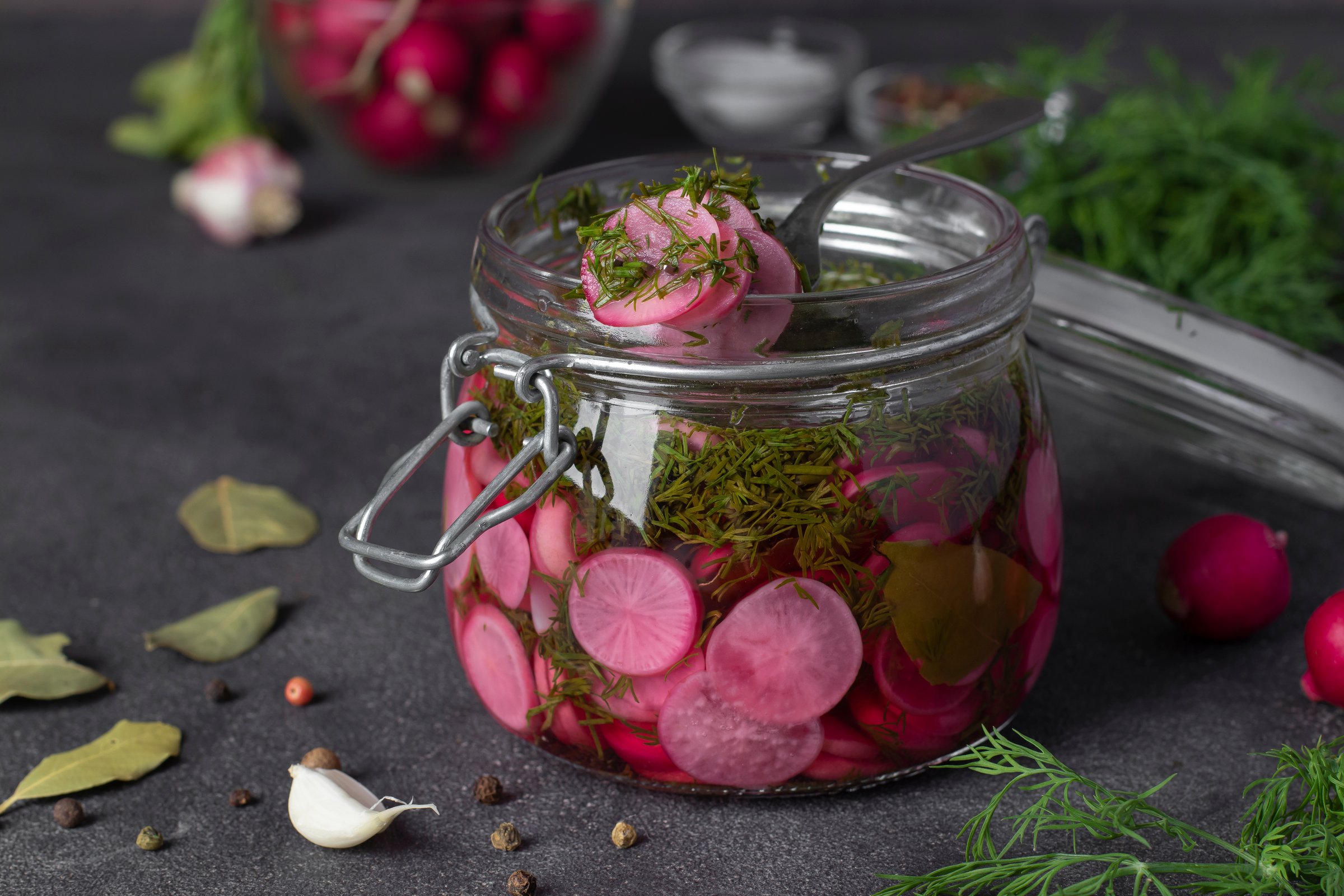 Marinated sliced radish with dill and garlic in open glass jar on gray table, Close-up