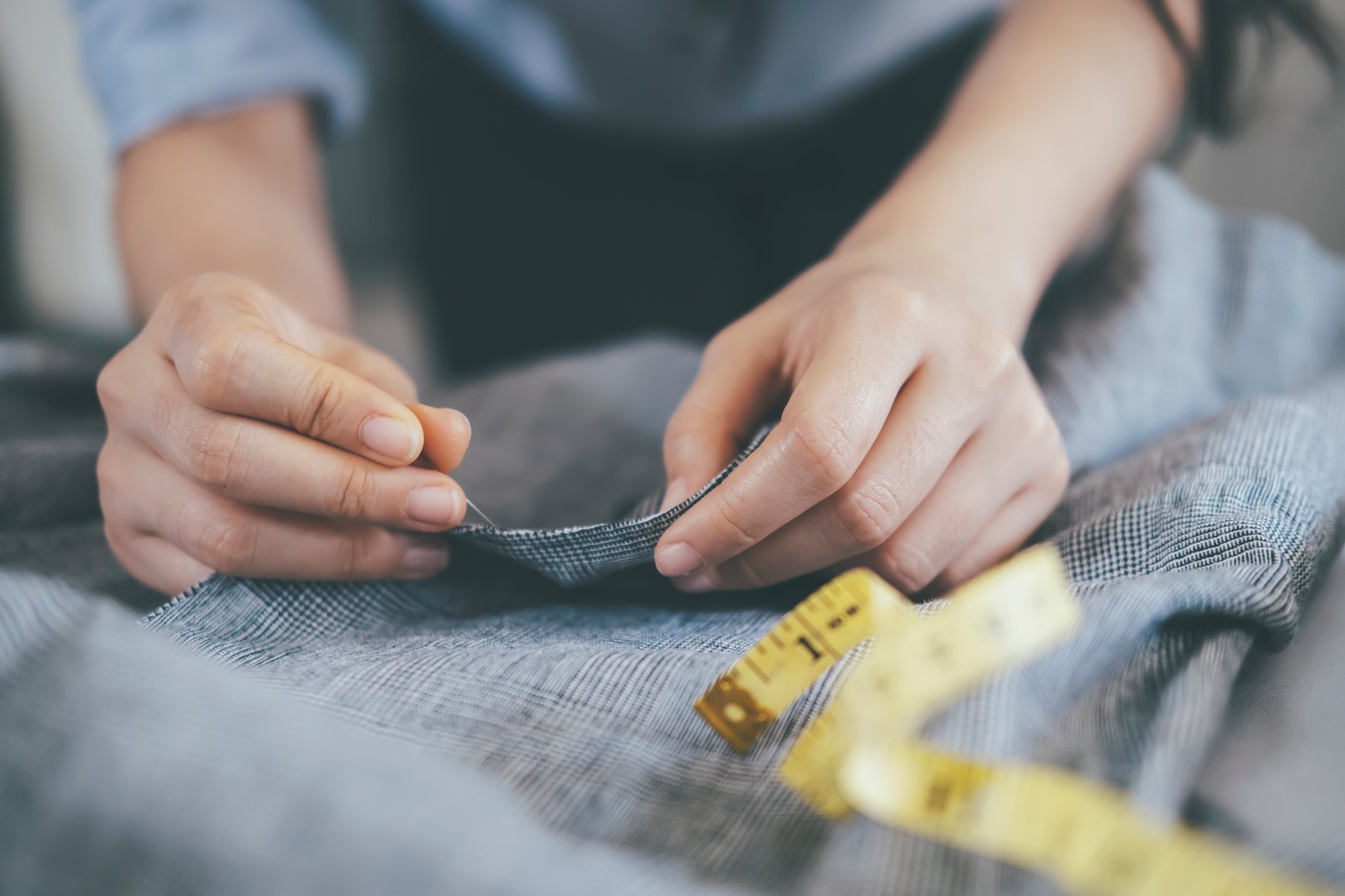 Closeup young woman tailor sawing jacket on on working table.