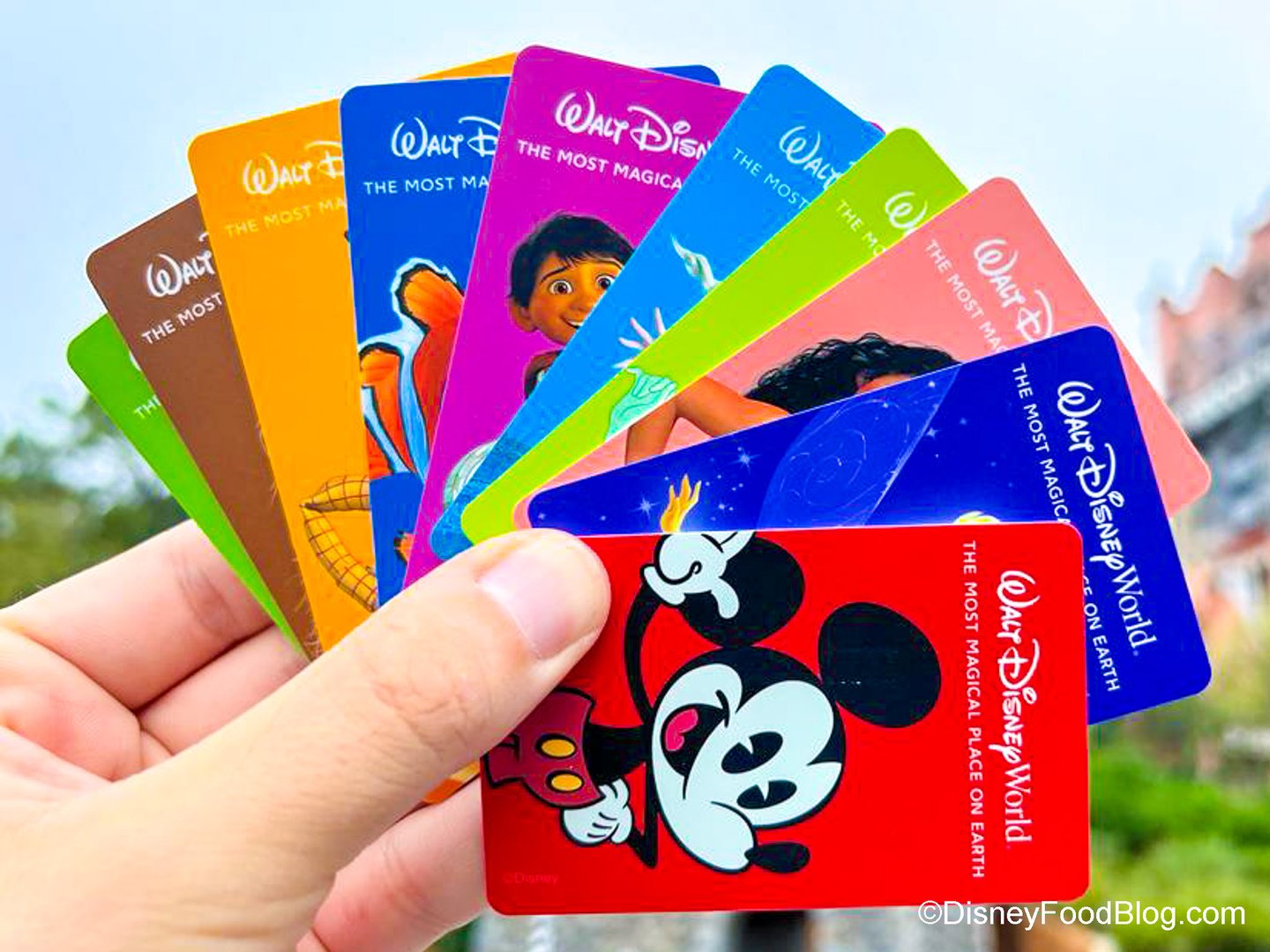 A hand holds various colorful Walt Disney World tickets featuring characters like Mickey Mouse and others.