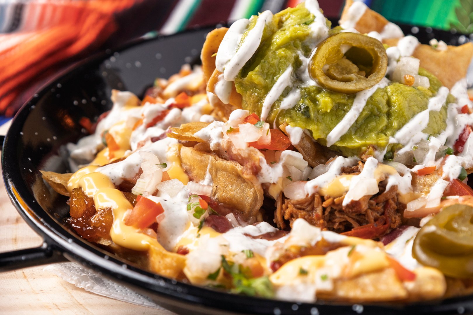Delicious nachos with guacamole, jalapeños, sour cream, and pico de gallo being served on a black plate