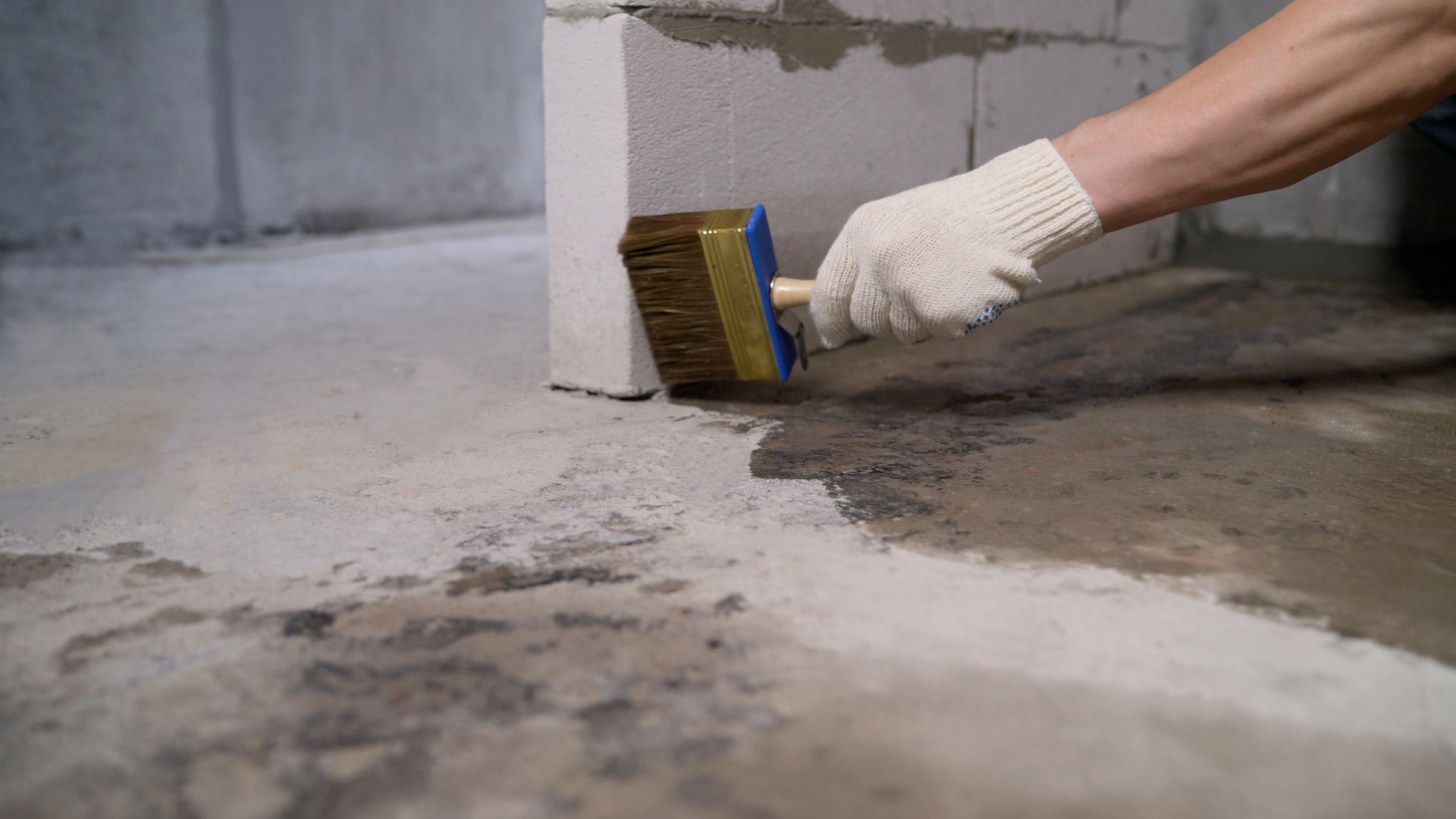 Construction worker applying a waterproofing membrane to a concrete floor using a brush, ensuring long-lasting protection against moisture