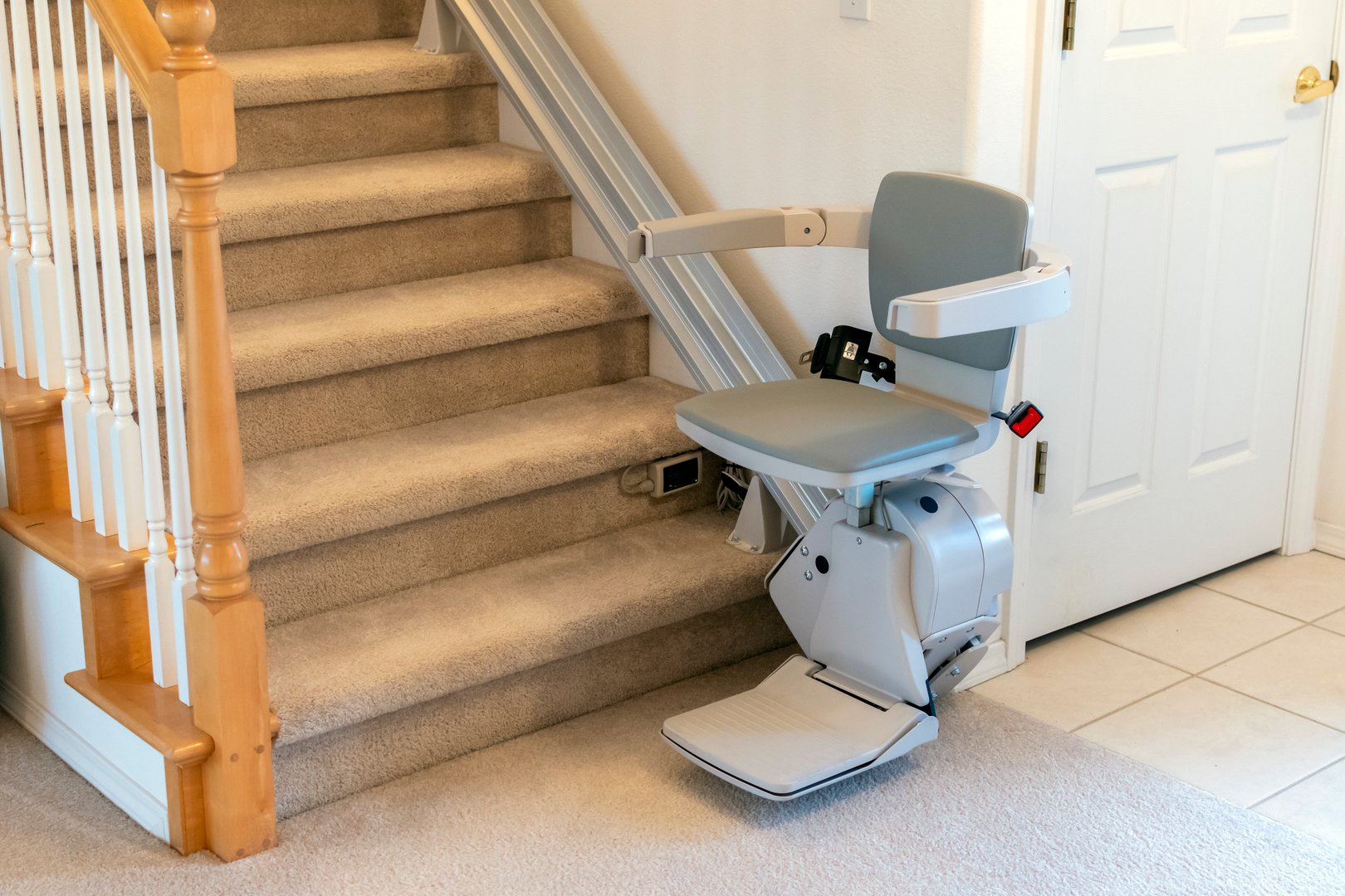 An electric, motorized chair or stair lift for persons with disabilities on a carpeted staircase in a two story residential home. A stair lift has a seat that the person sits on to ride up the stairs.