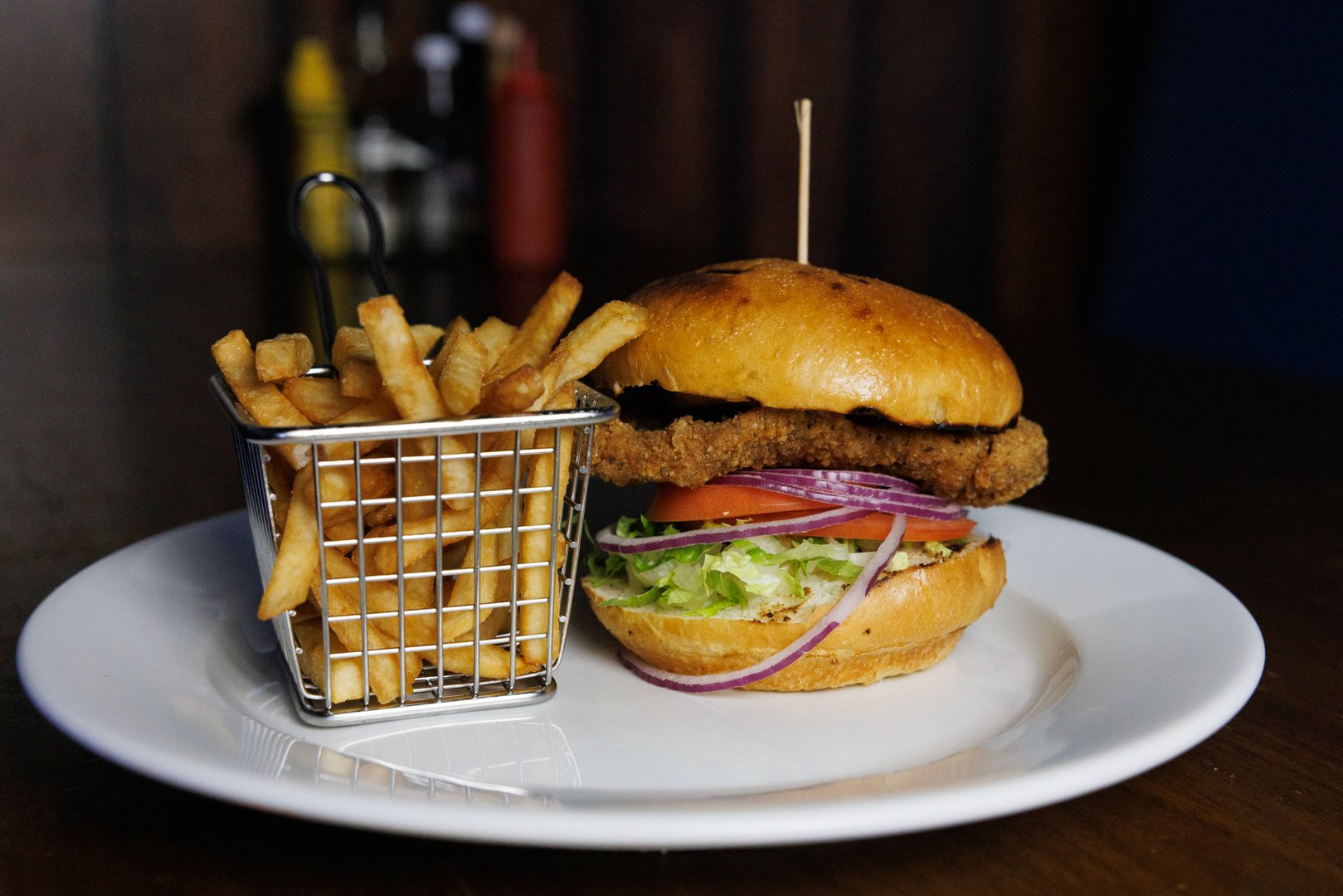 Chicken burger with fries in a stainless steel basket on a white plate in a bar / pub