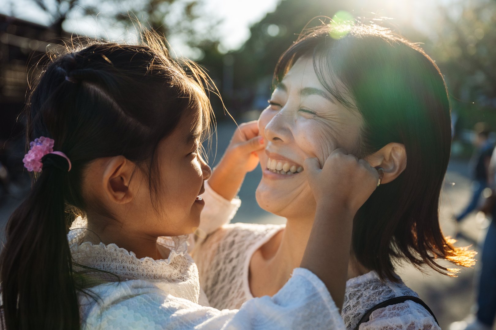 Playful daughter pulling cheeks of her laughing mother, having fun together on a sunny day at a park in tokyo, japan, creating a heartwarming moment of family bonding
