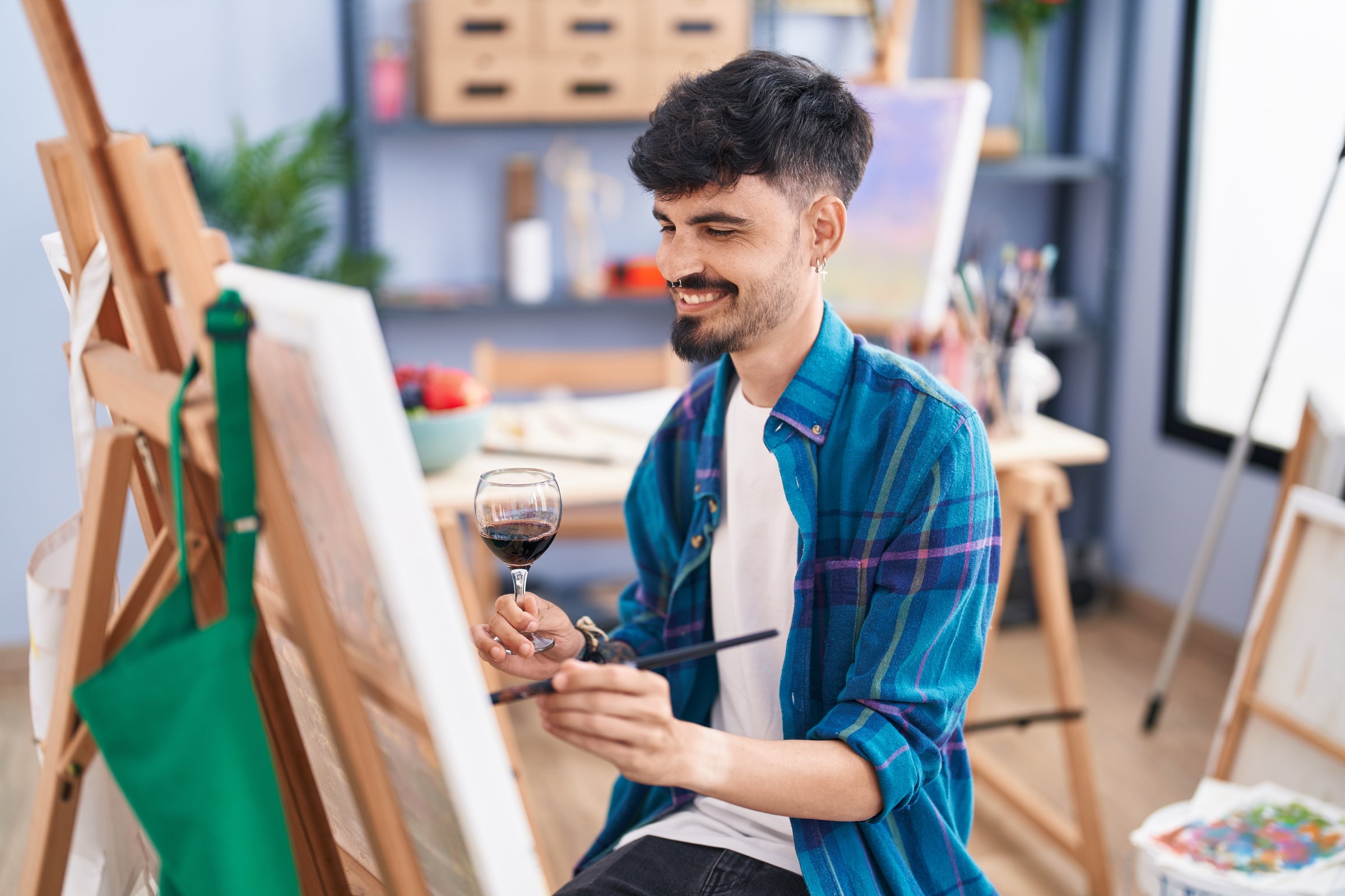 Young hispanic man artist drinking wine drawing at art studio