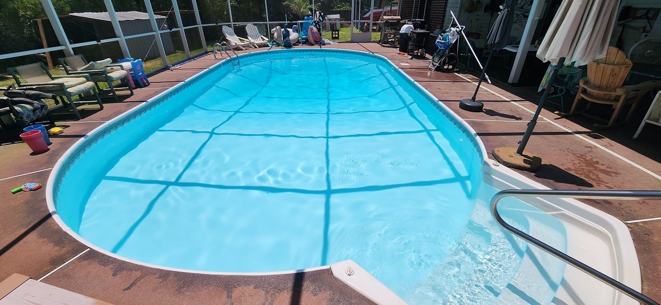 Pool cleaner with blue uniform cleaning poolside with brush on sunny summer day at luxury hotel resort