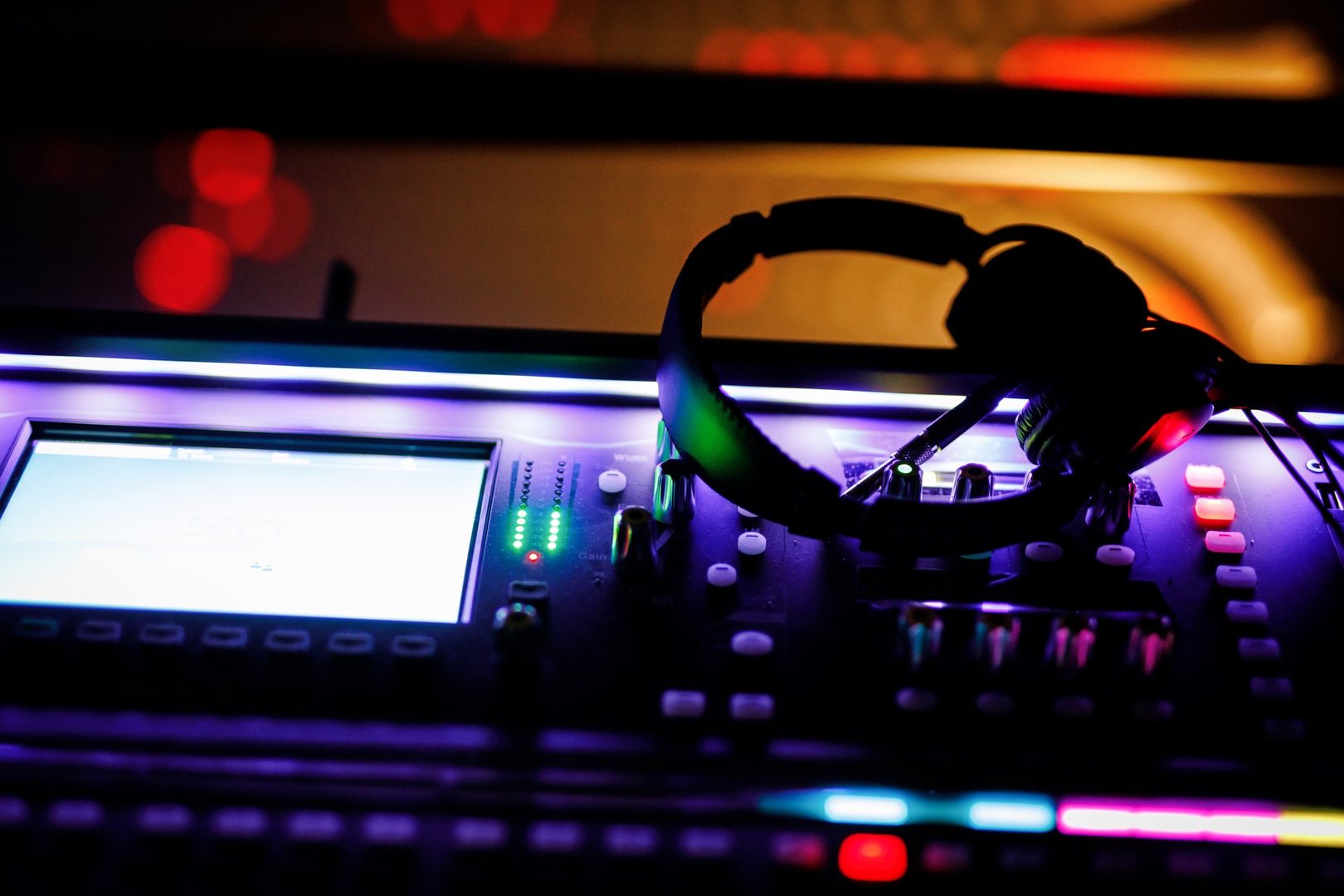 Headphones rest on an illuminated DJ console, highlighting audio mixers and controls.