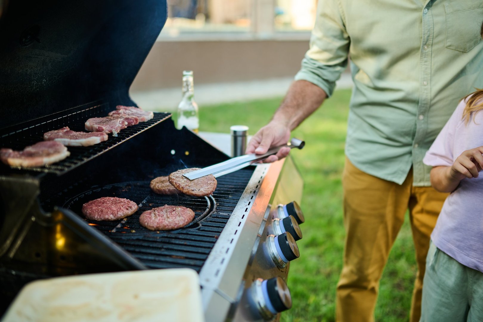 Dad grilling burgers and steaks in the backyard on a sunny day, kids playing, creating a fun family cookout
