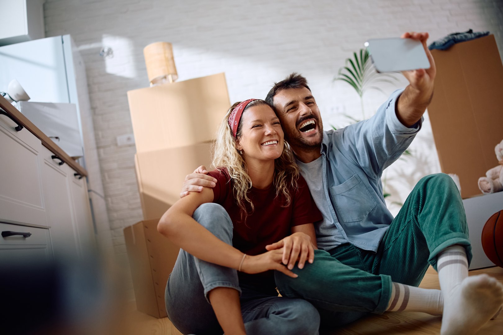 Happy couple taking selfie with cell phone while having fun in their new home.