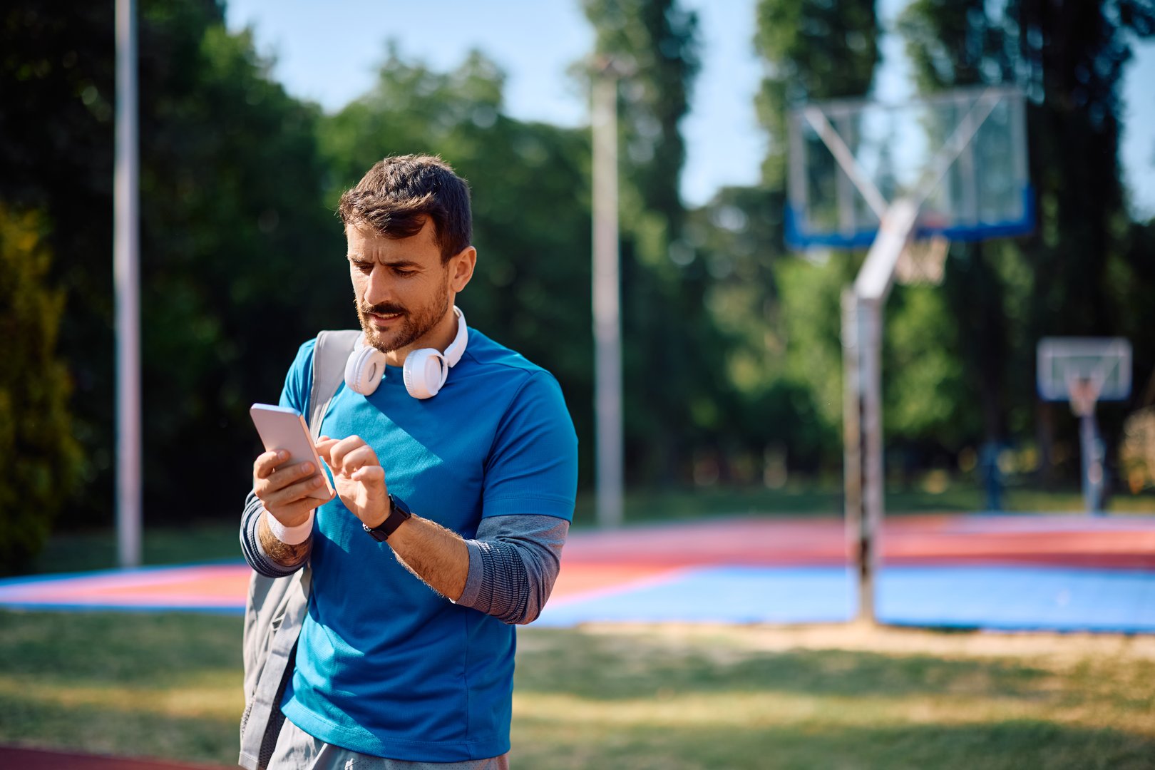 Male athlete texting on mobile phone while exercising outdoors. Copy space.