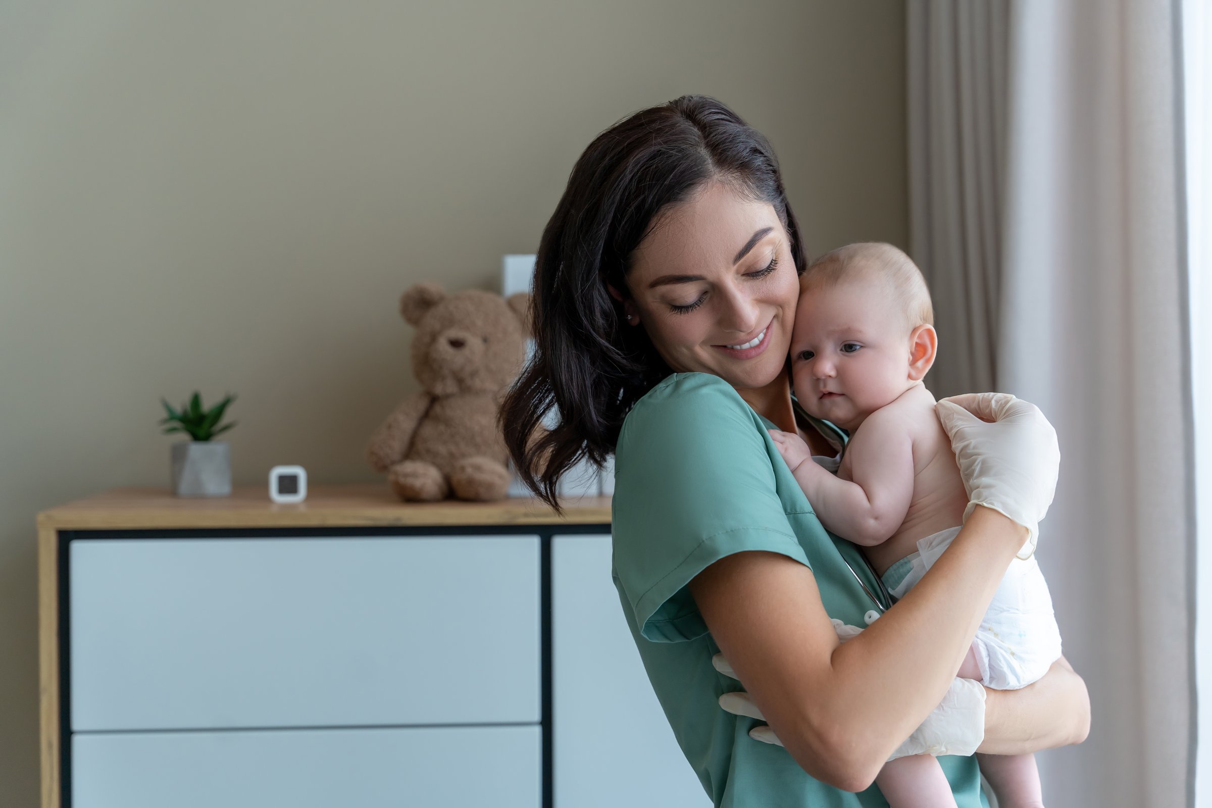 Beautiful young nurse medical worker in gloves holding newborn baby in hands
