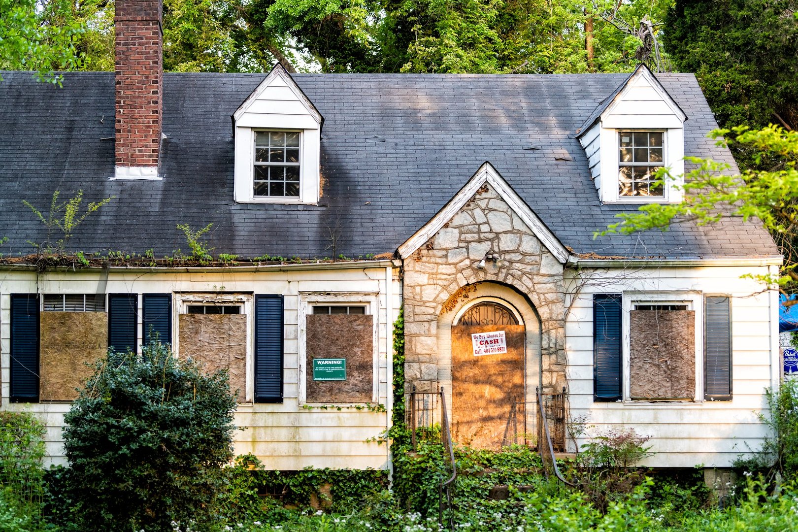 Atlanta, USA - April 21, 2018: Old abandoned weathered wooden house with entrance and notice sign warning and company buying for cash and number
