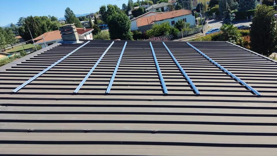 A corrugated metal roof with vertical support rails, surrounded by trees and residential buildings.