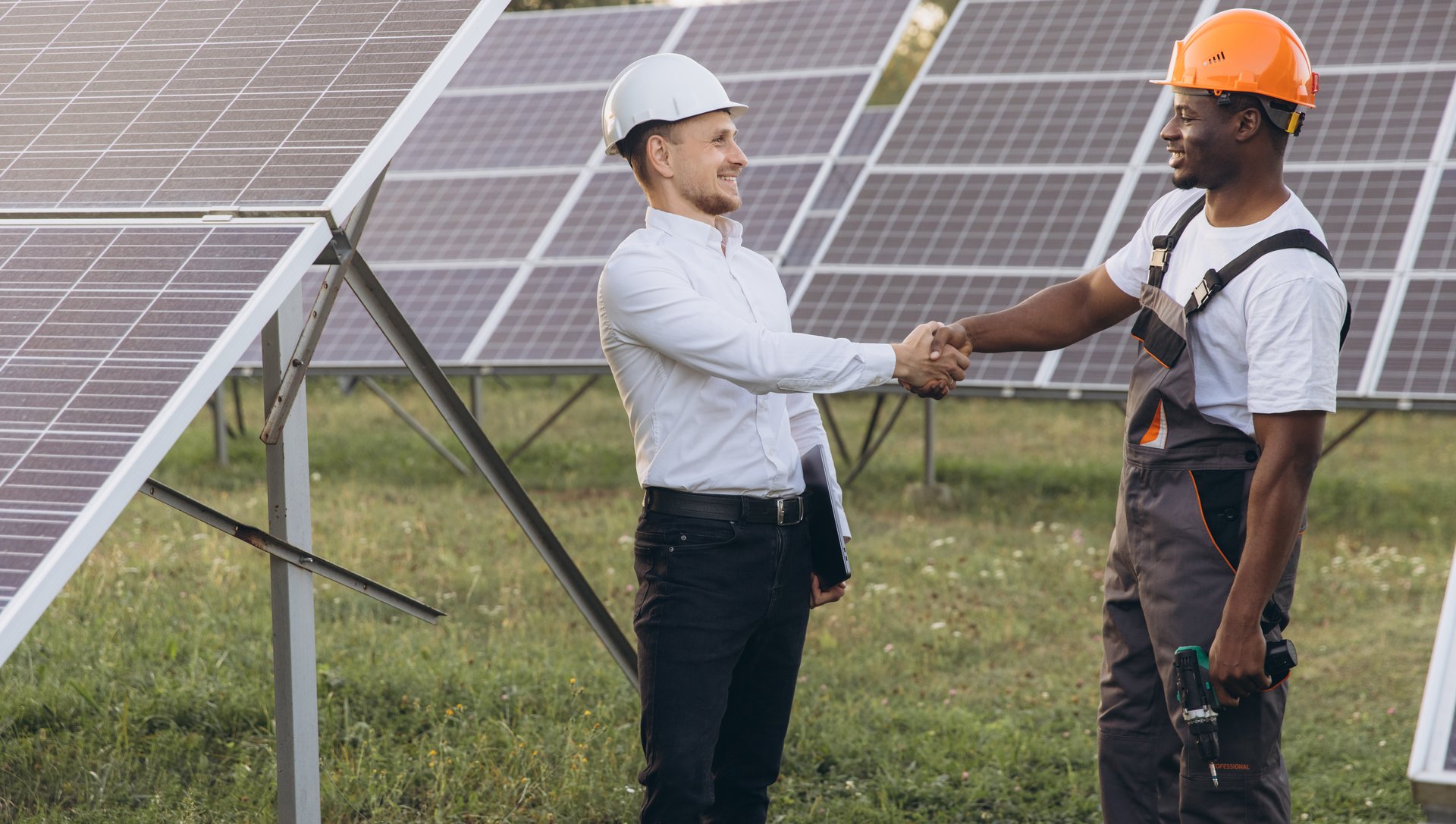 Two engineers, wearing helmets, shake hands in front of solar panels, symbolizing teamwork and renewable energy. They represent collaboration and innovation in the solar energy industry.