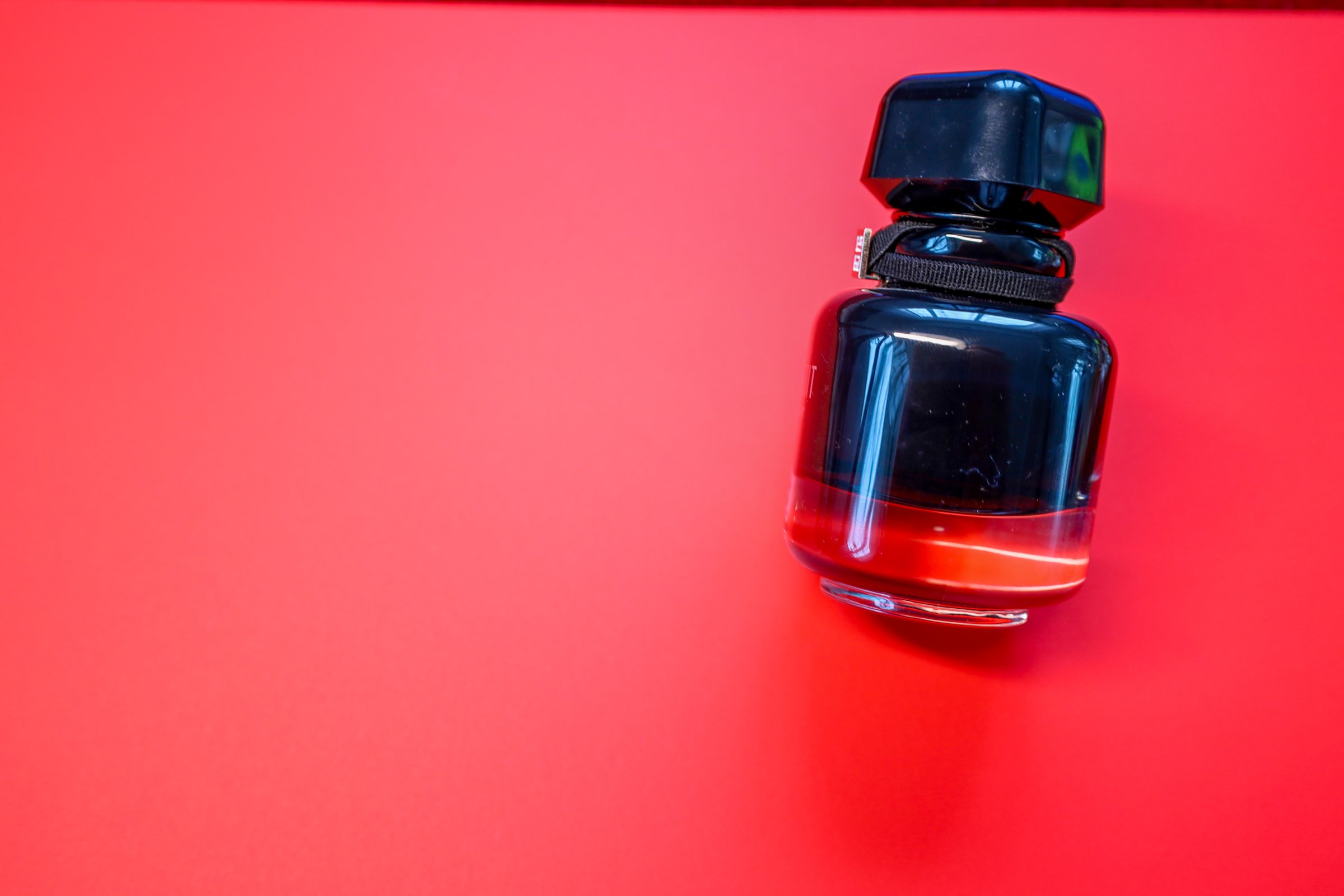 A stylish black perfume bottle with red liquid is placed on a bright red background