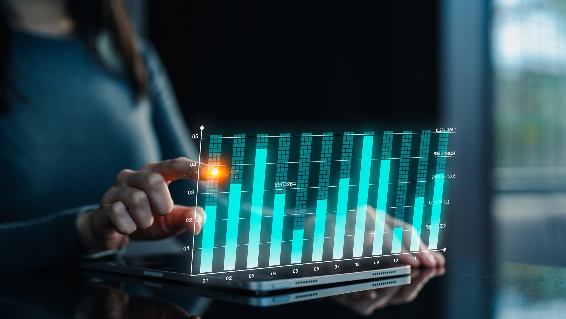 A person interacts with a digital tablet displaying a glowing, futuristic bar chart hologram in a dark room with natural light in the background.