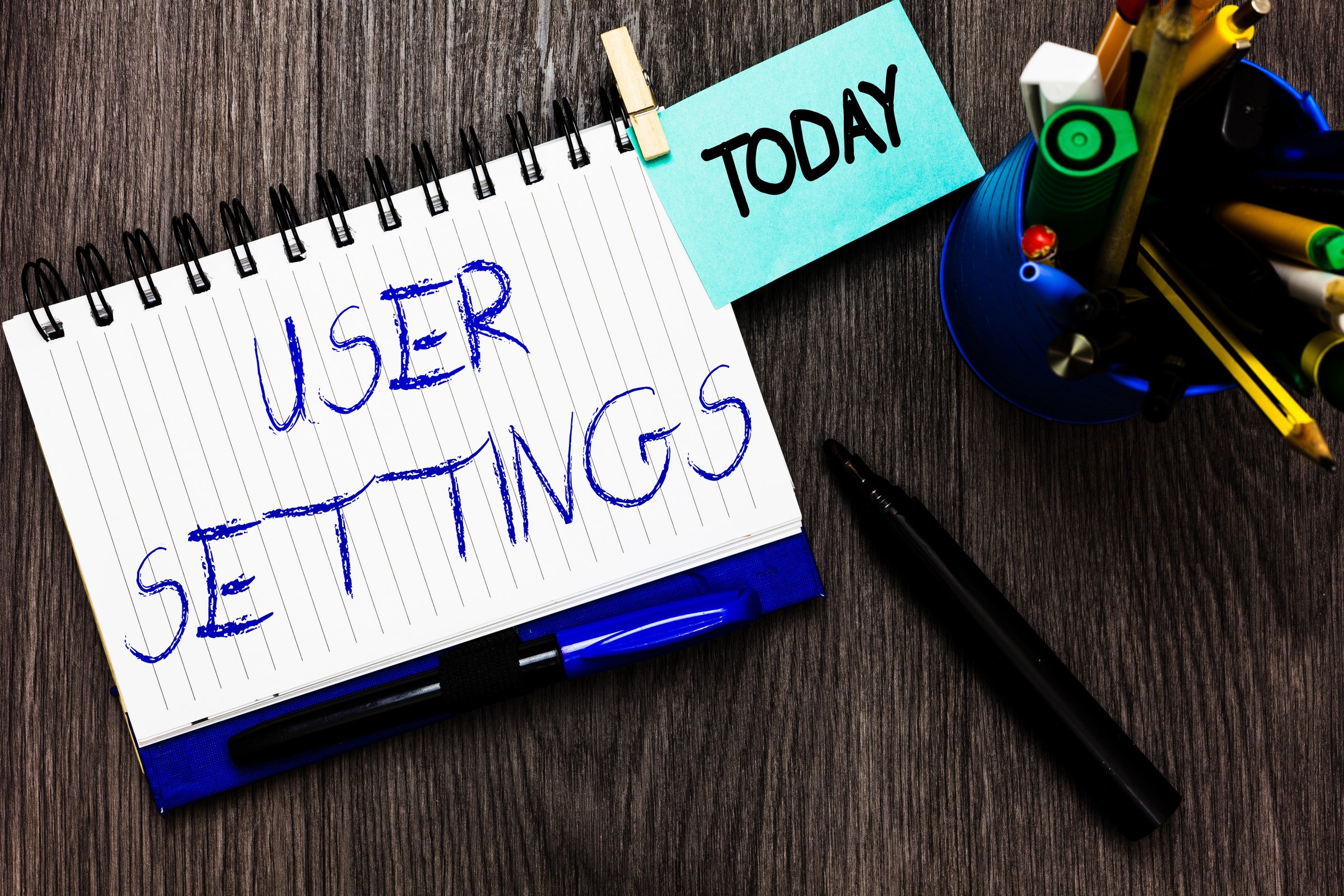 Handwriting text User Settings. Concept meaning Configuration of appearance Operating System Personalized Open notebook clothespin holding reminder cup markers wooden background