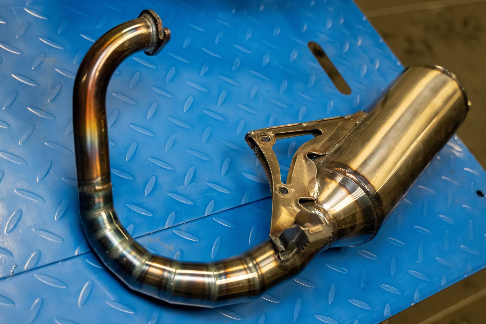 Motorcycle exhaust system placed on a blue metal background in a workshop
