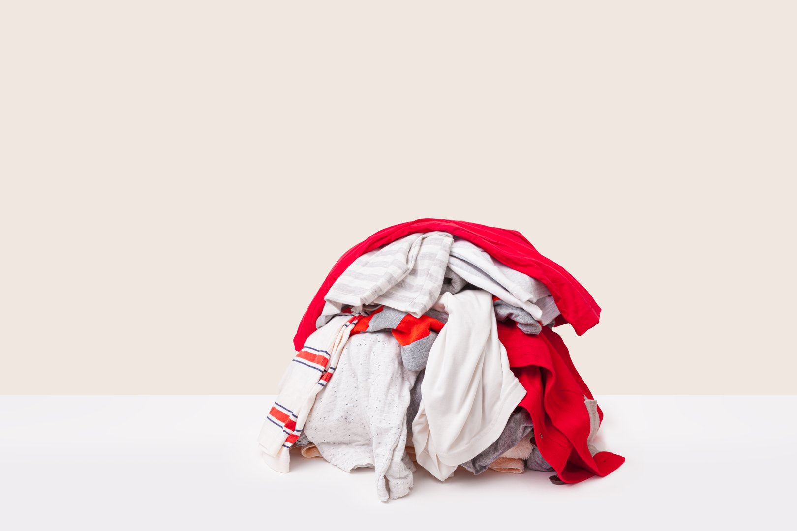 Stack of red dirty clothes waiting for laundry isolated on light beige background