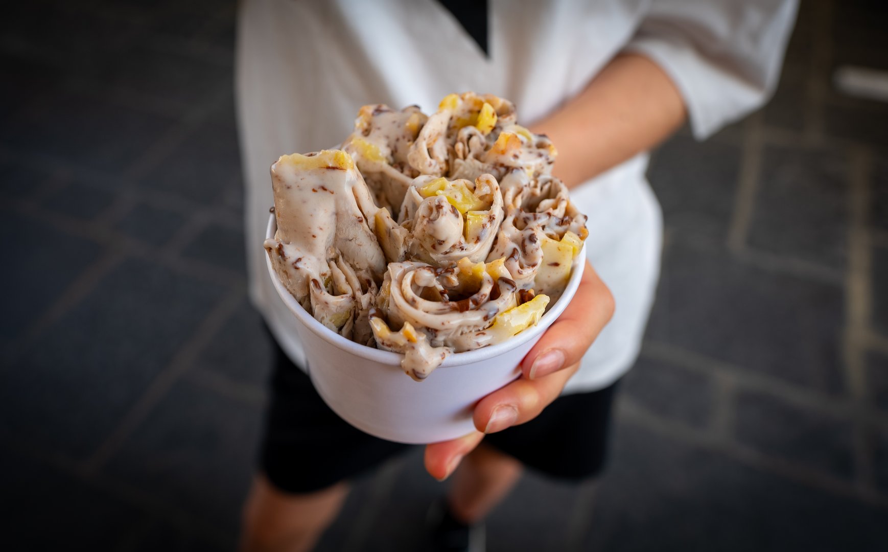 Rolled ice cream in cup in girl hands at street.