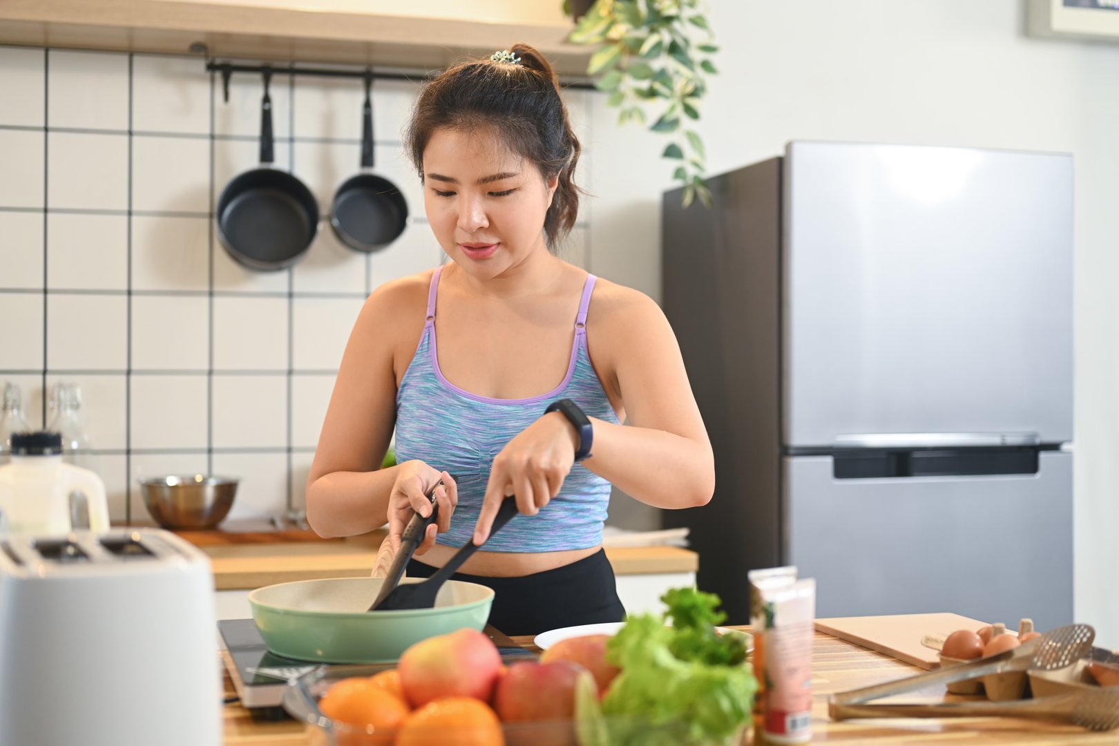 Sporty young woman preparing healthy food for breakfast in kitchen after doing workout at home.