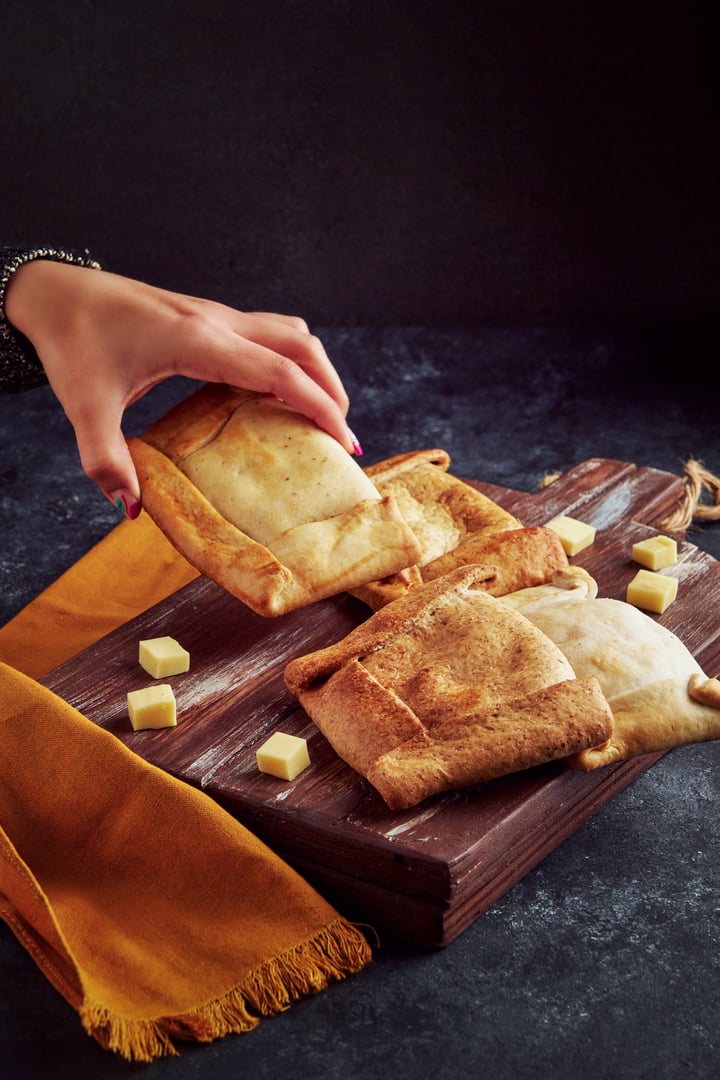 Woman's hand holding a whole wheat Chilean empanada on a chopping board