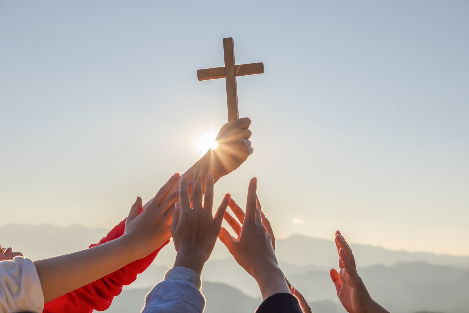 Silhouette family hands praying and holding Christian cross for worshipping God on mountain at sunrise background. Christian, Christianity, Religion copy space background. Easter Sunday concept: