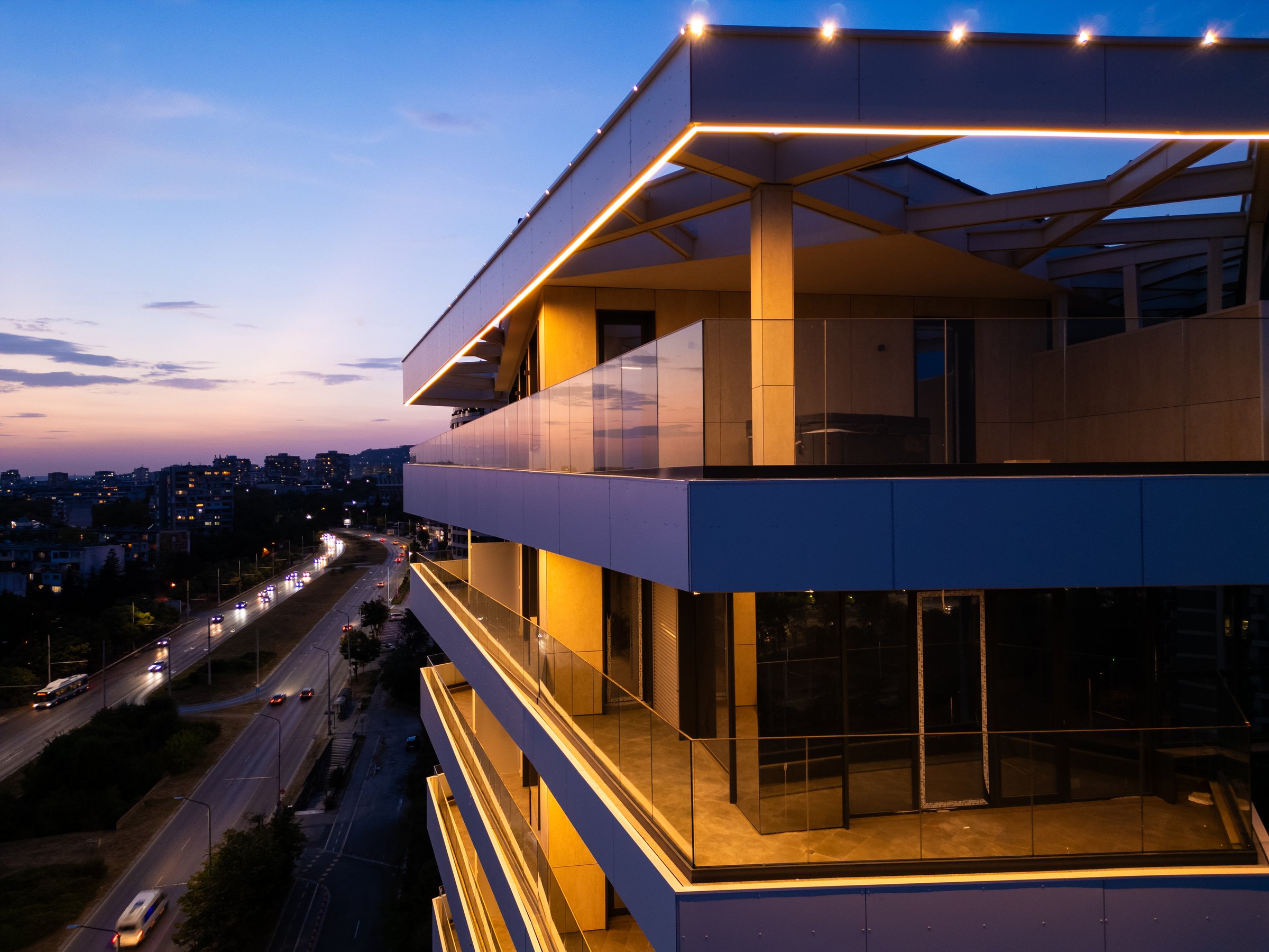 Aerial drone shot of a modern building facade illuminated by sleek LED lighting at dusk, capturing the contrast between the urban night skyline and contemporary architecture.