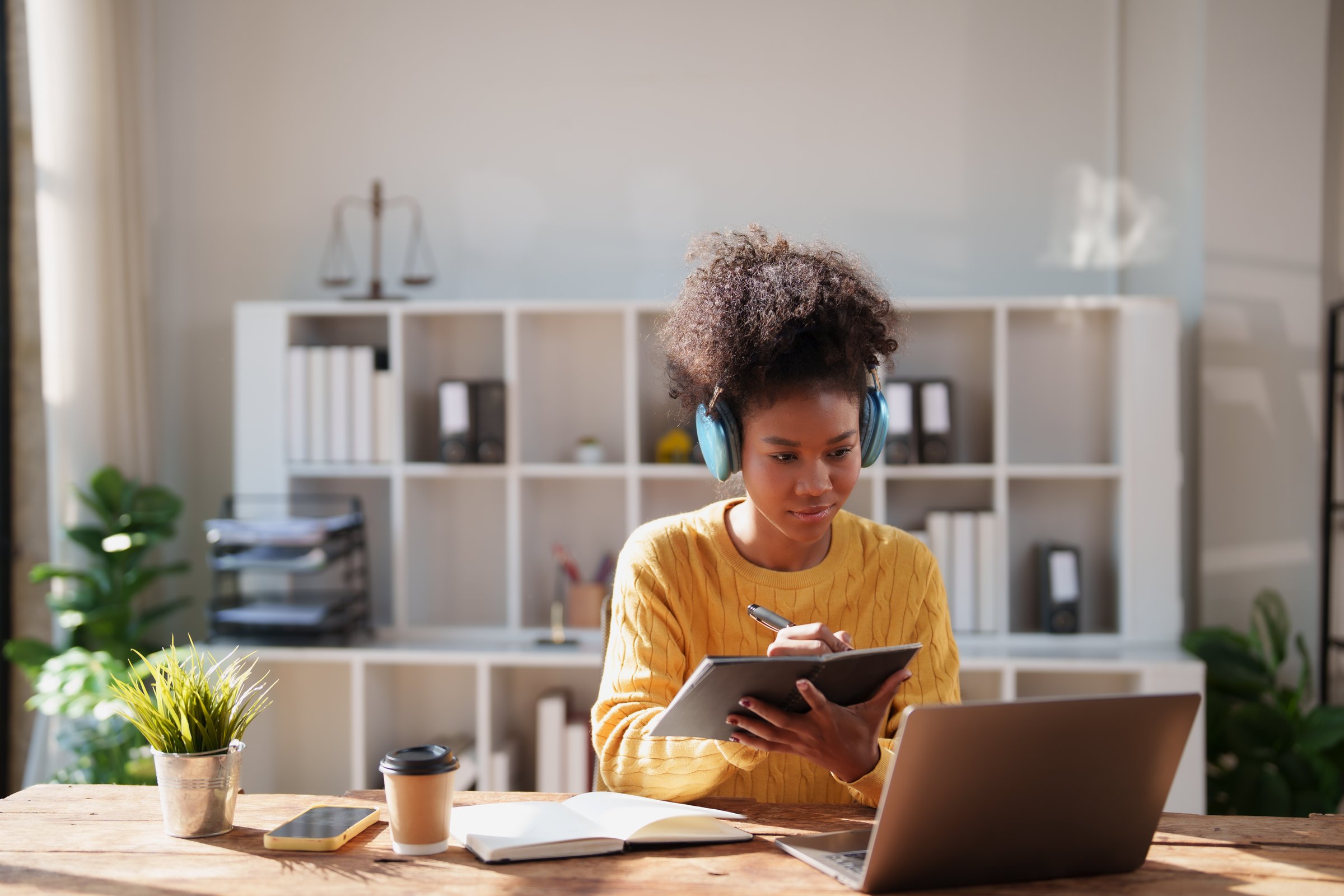 Young Black woman with headphones studying at a bright home office desk