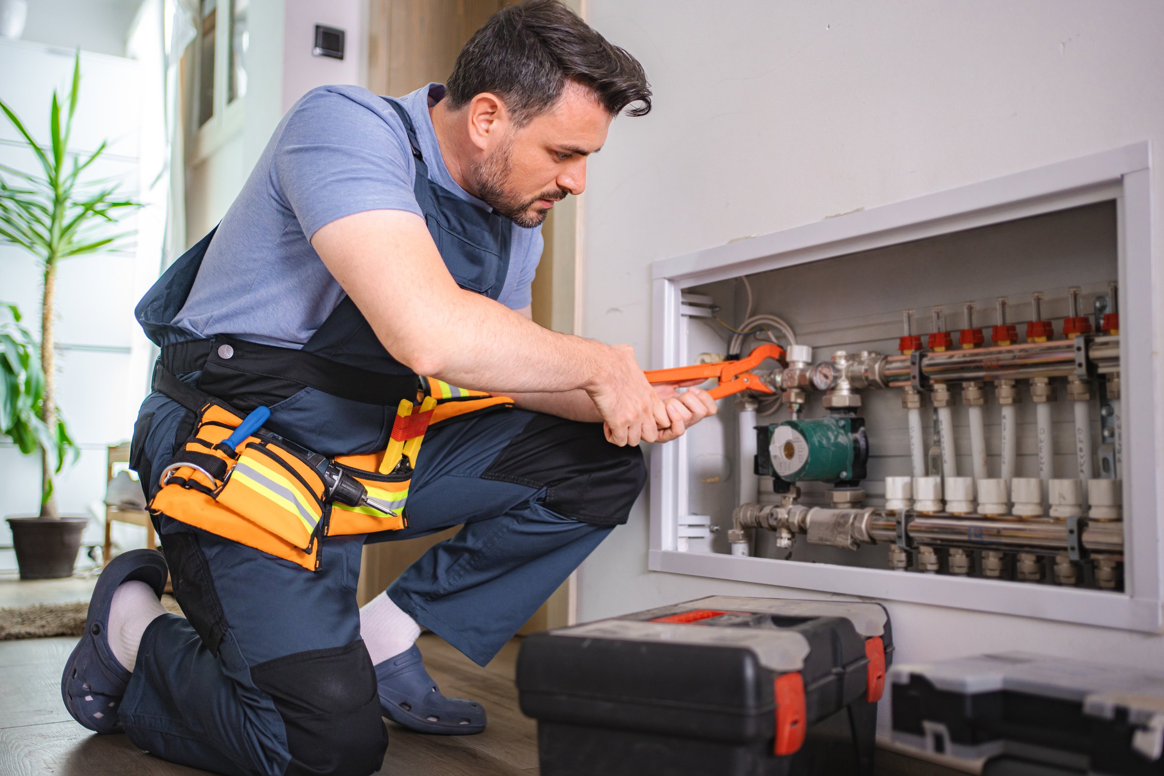 Professional plumber working on underfloor heating installation in a modern house, using adjustable pliers