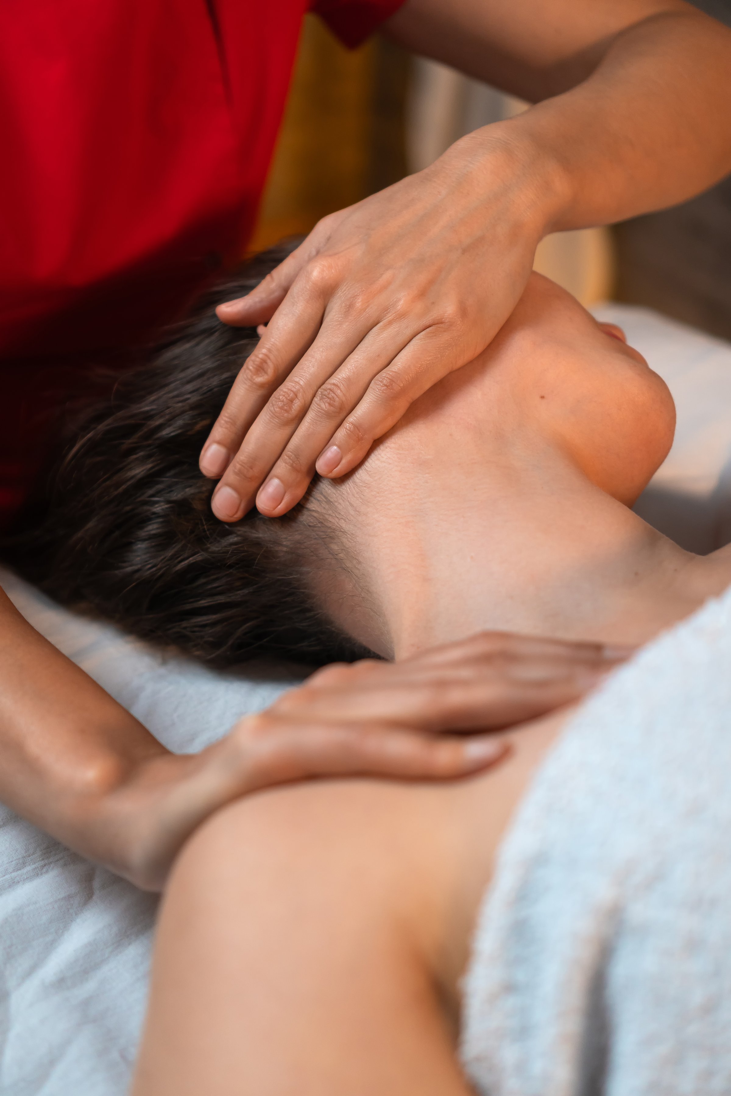 Massage therapist in a red suit gives a relaxing neck and shoulder massage to a young woman at a spa or beauty salon. Concept of a healthy body. Vertical photo