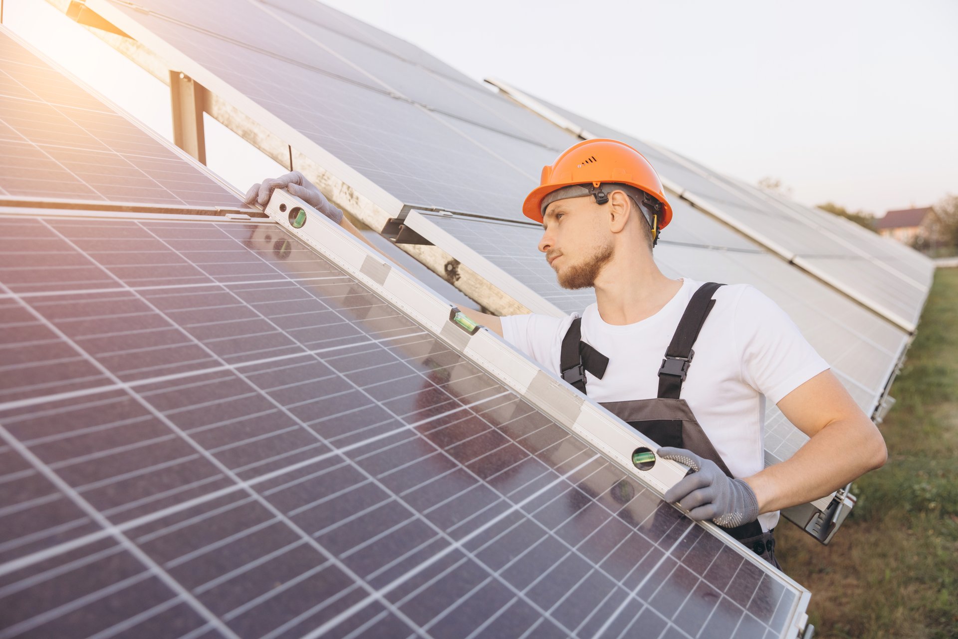 A male engineer in a hard hat inspects solar panels using a level tool. The image emphasizes renewable energy and solar technology in an outdoor setting.