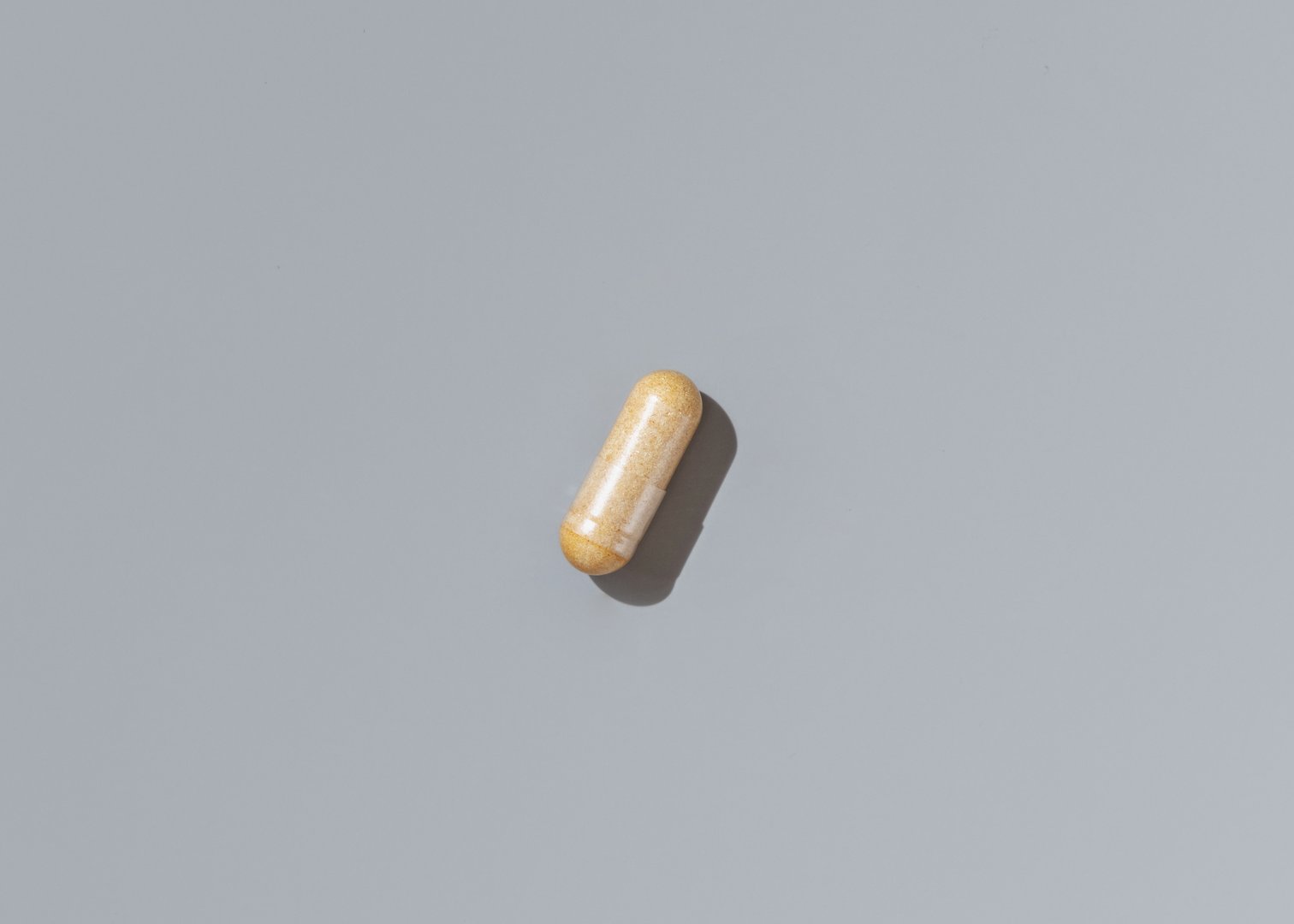 Yellow medical capsule on grey top view, hard shadows. Preventive medicine and healthcare, taking dietary supplements and vitamins.  Minimal composition
