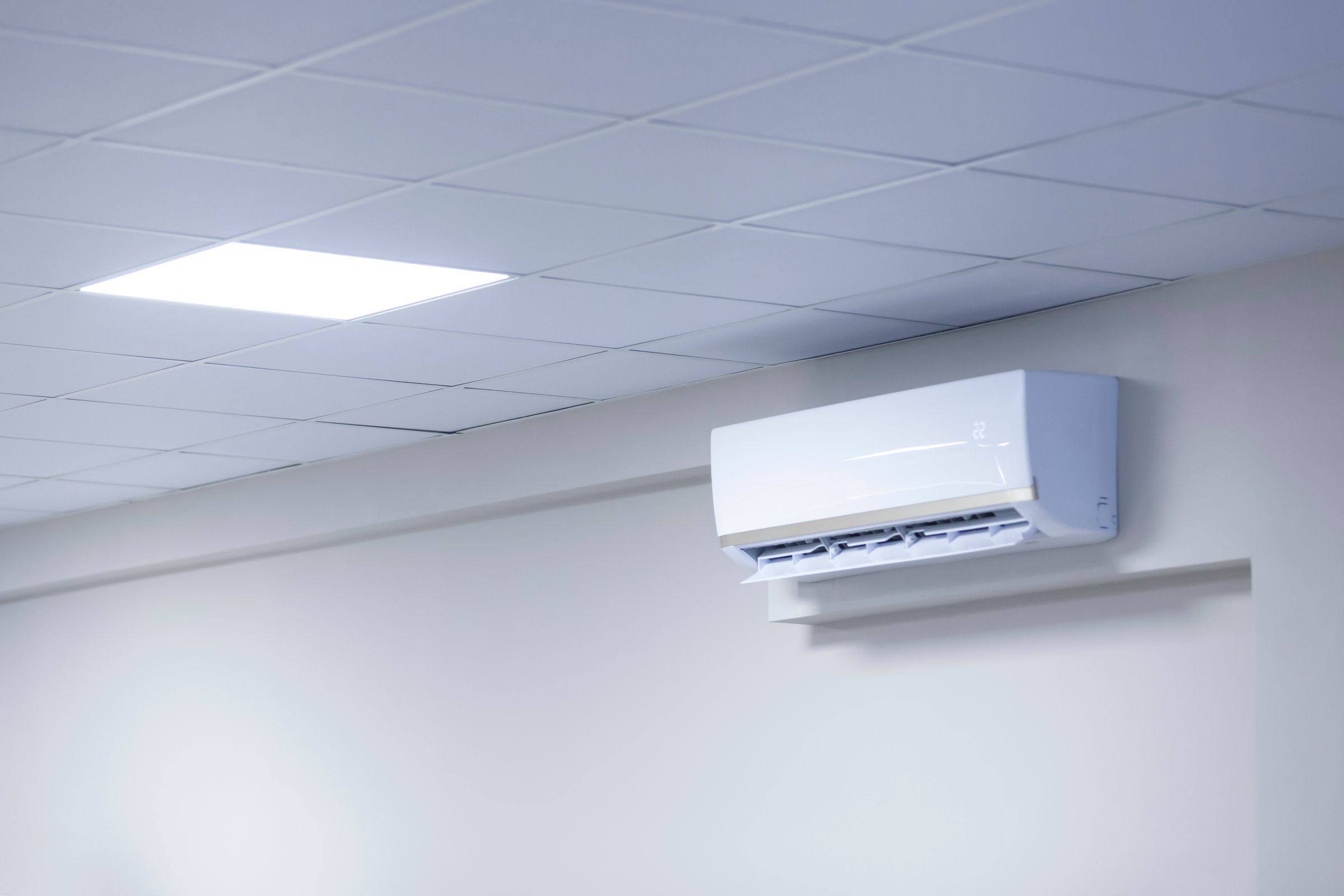 A wall-mounted air conditioner in a room with a tiled ceiling, showcasing modern climate control technology. Copy space.