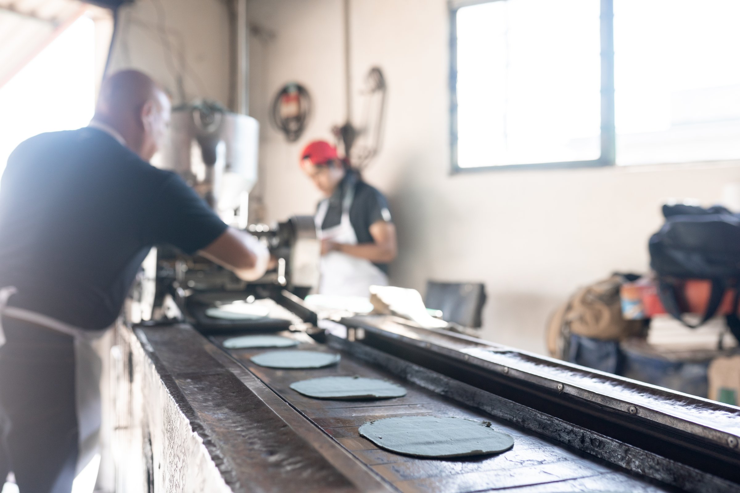 An adult man is working with his son producing blue corn tortillas with a nixtamall mill. Concept of traditional corn tortillas preparation