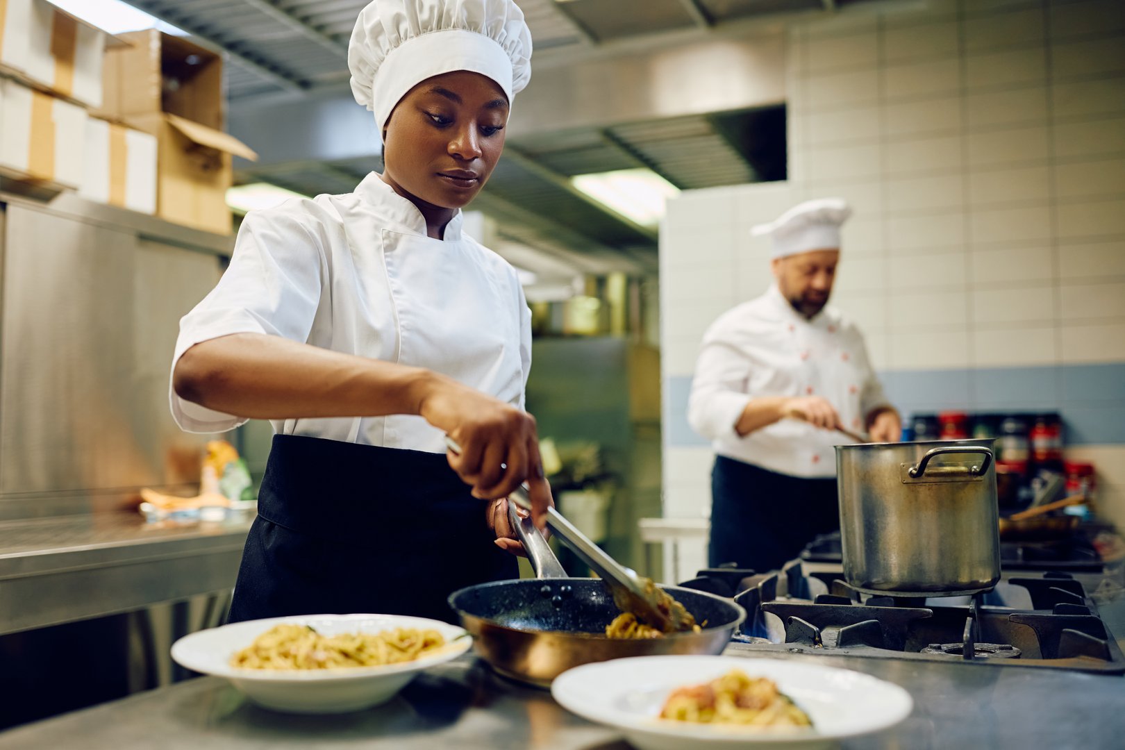African American female chef serving food while working in a restaurant kitchen.