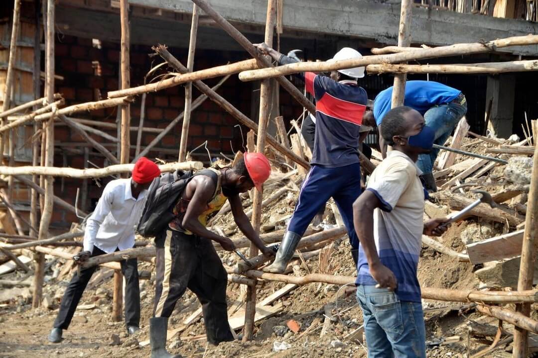 Construction workers building a wooden scaffold on a construction site, with tools and safety gear, in an urban setting.